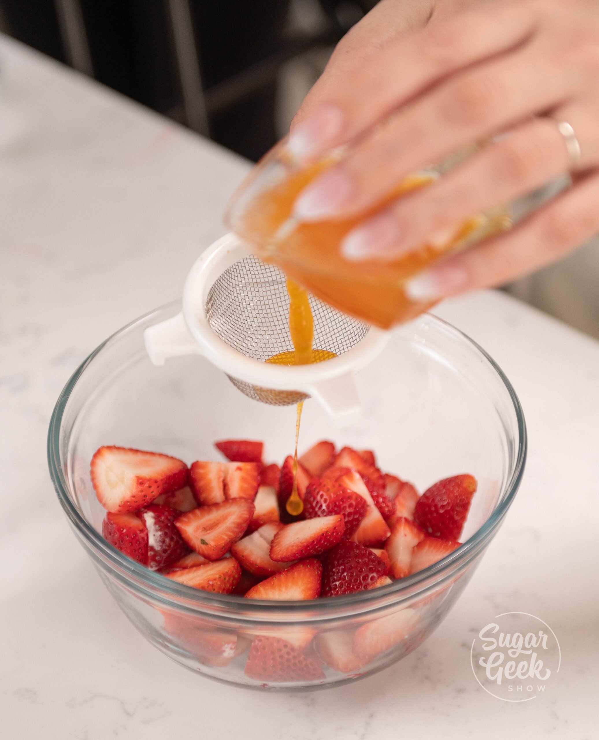 hand straining jam over bowl of strawberries