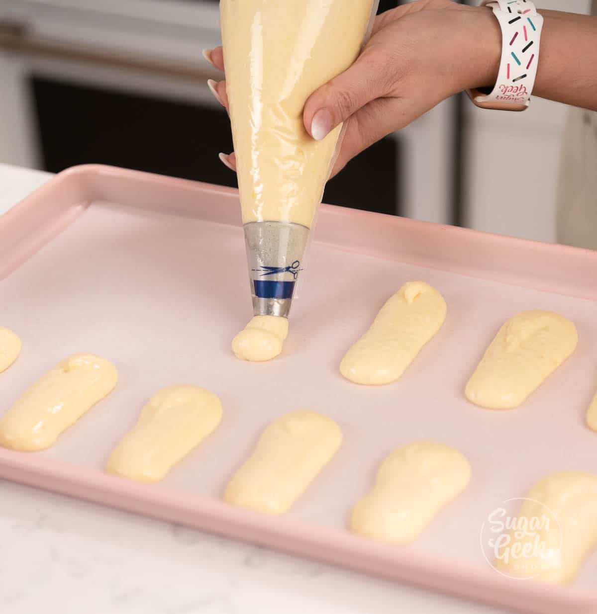 hand holding piping bag filled with batter piping cookies onto tray.
