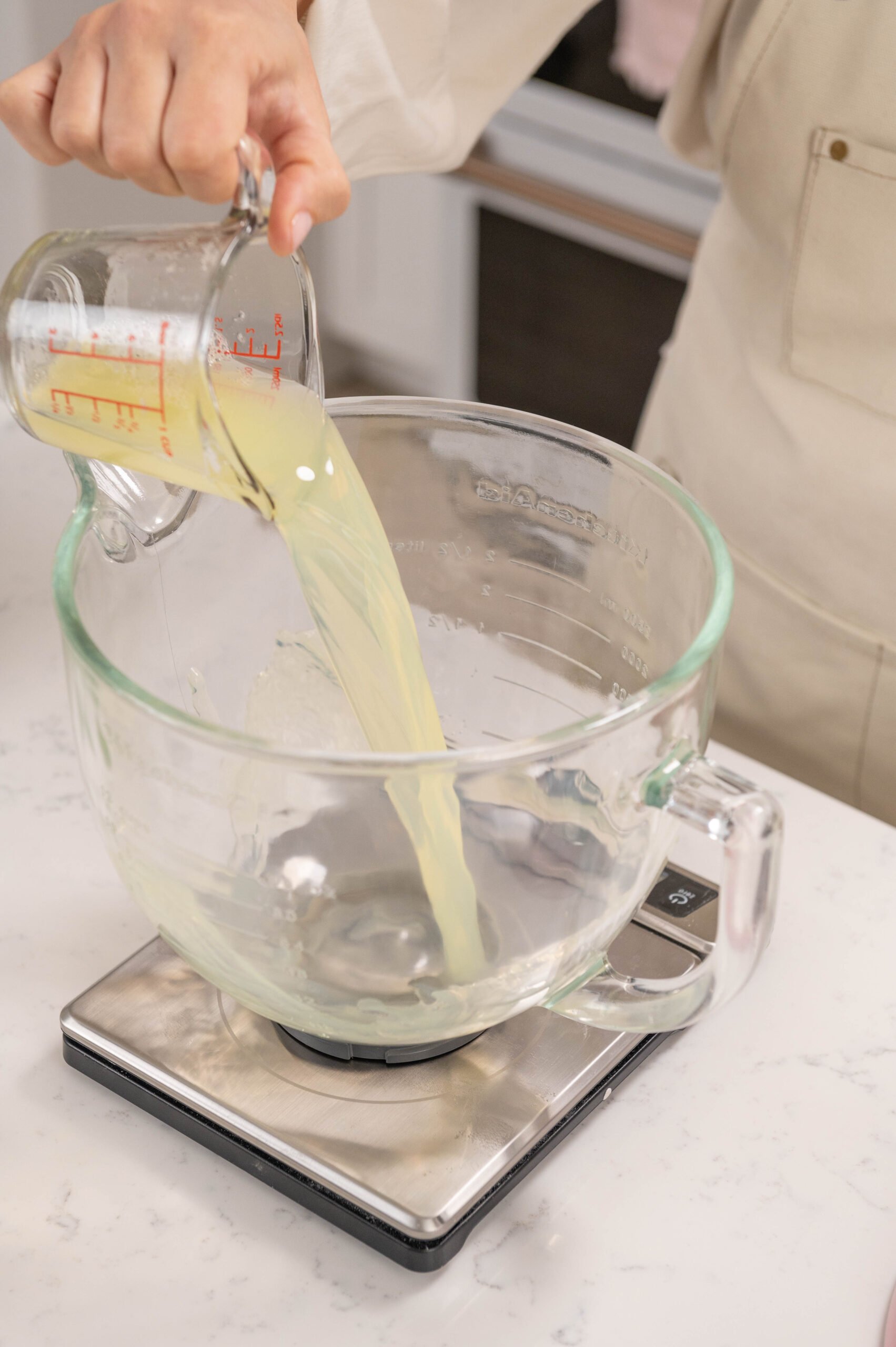 hand pouring a container of pasteurized egg whites into a glass stand mixer bowl