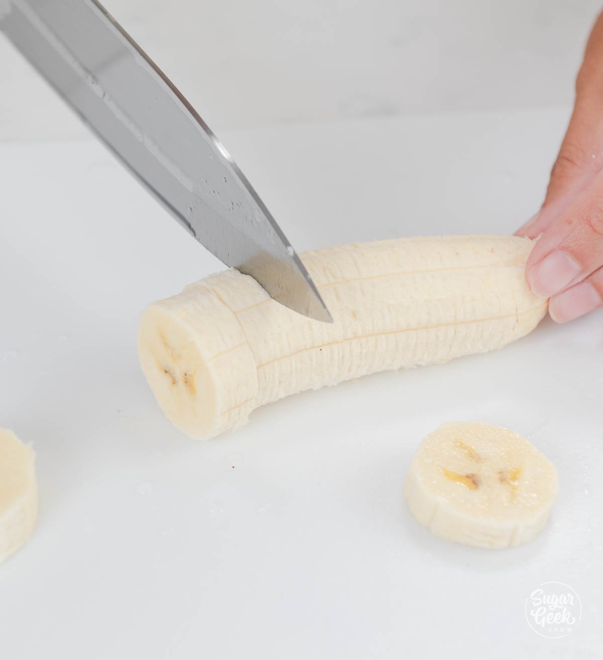 hand using knife to dice banana slices.