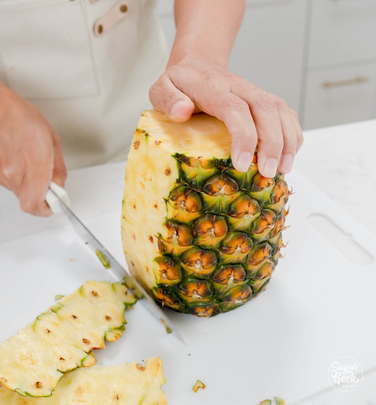 hand using knife to trim the sides of a pineapple. 