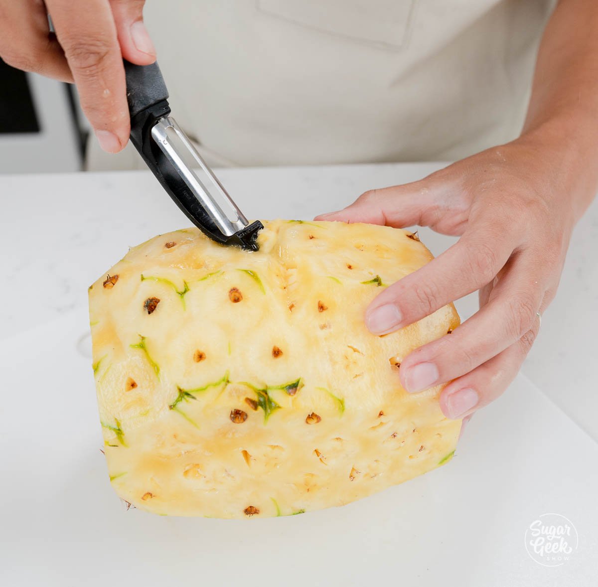 hand using potato peeling to peel pineapple. 