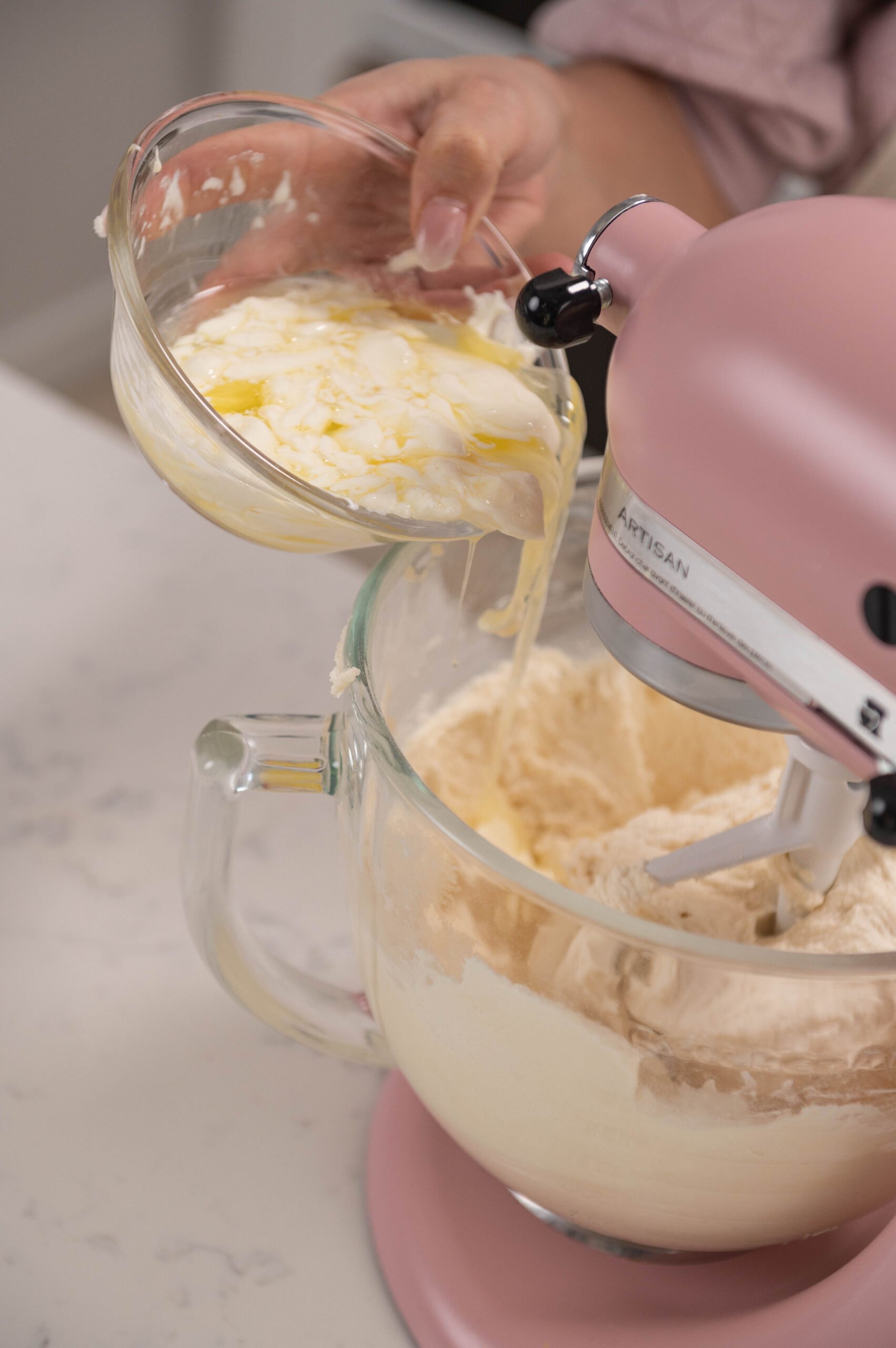 hand pouring bowl of egg whites into stand mixer bowl