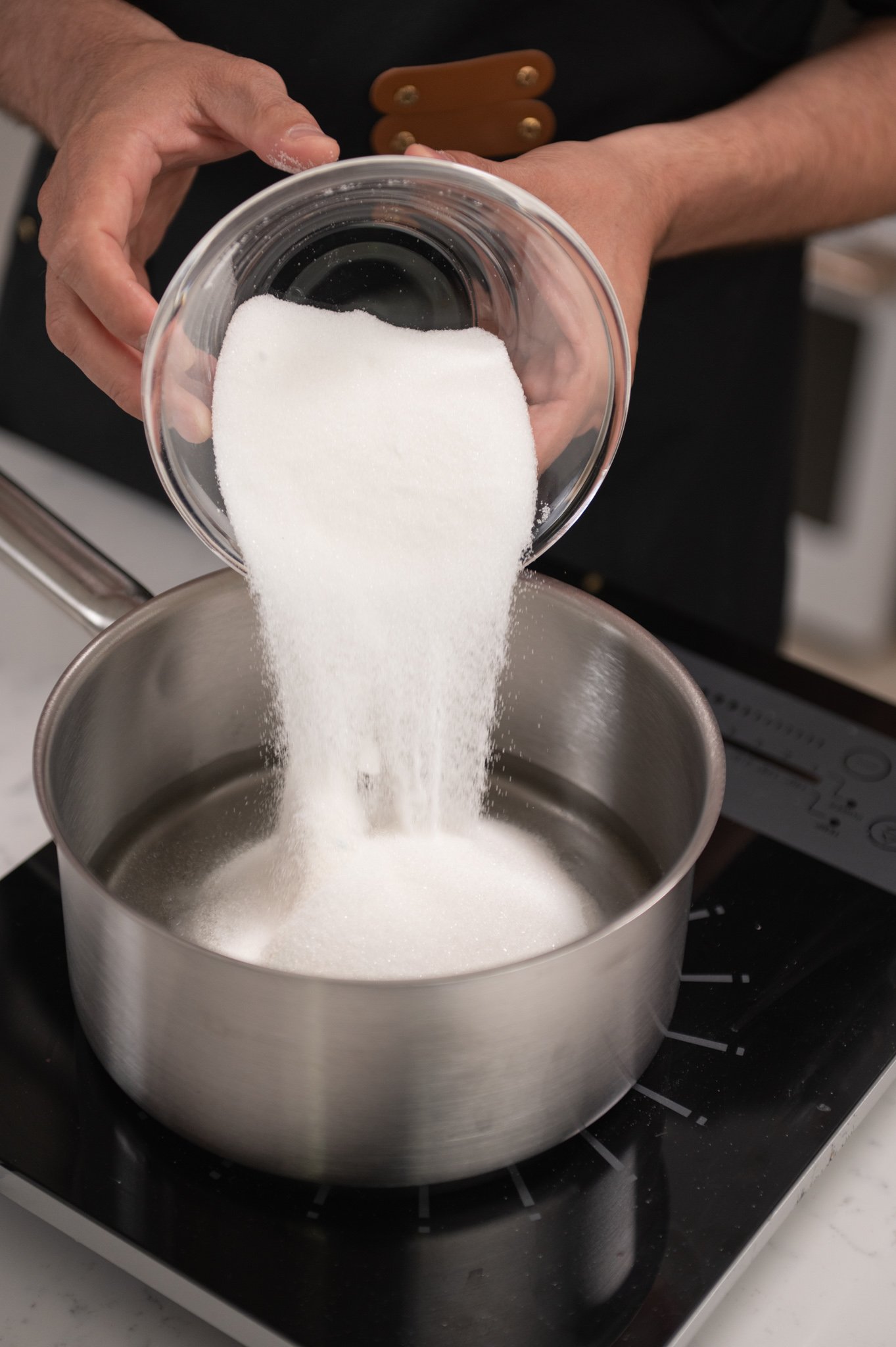 hand pouring bowl of sugar into pot.