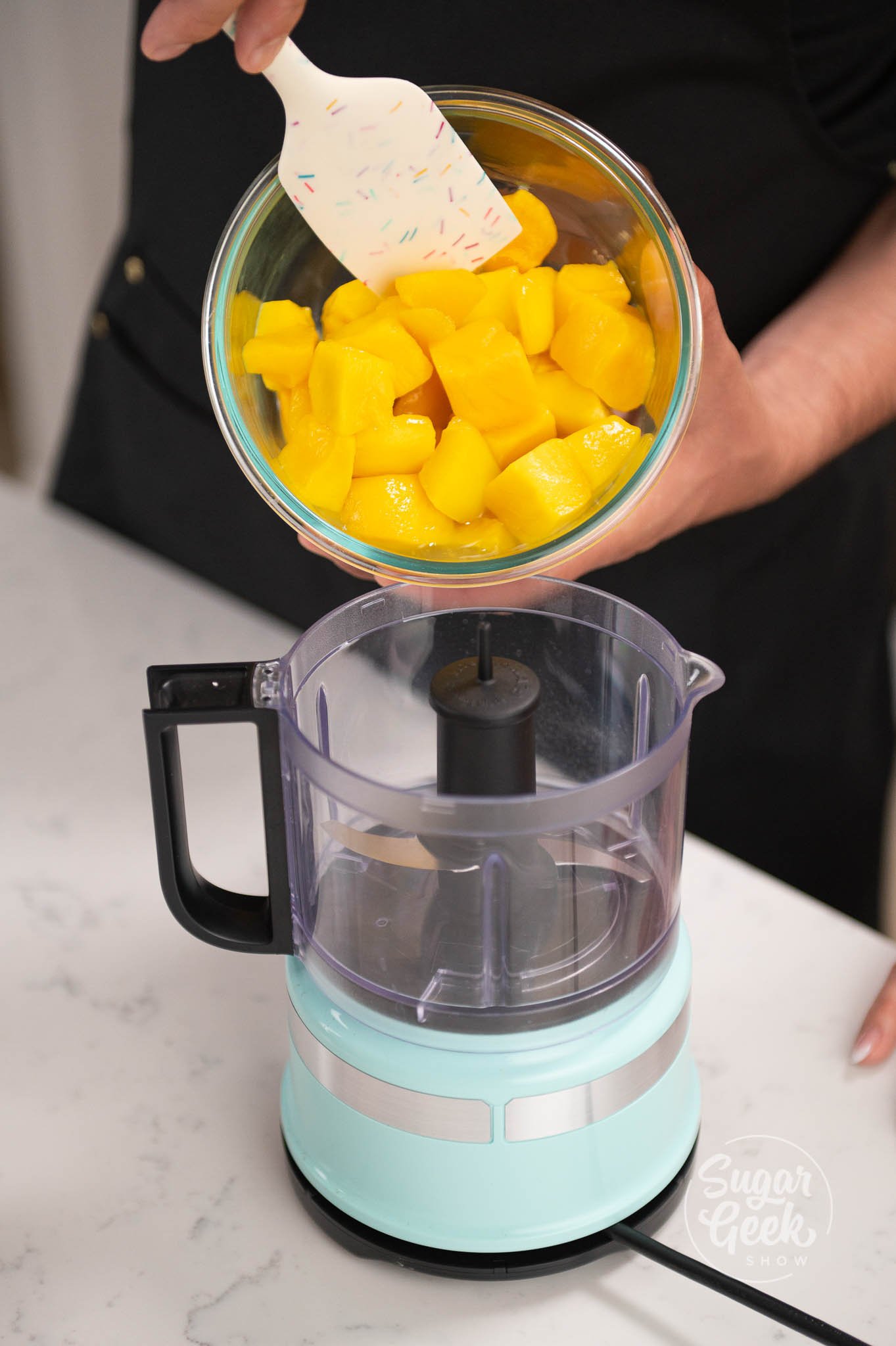 hand holding spatula scooping mango into blender
