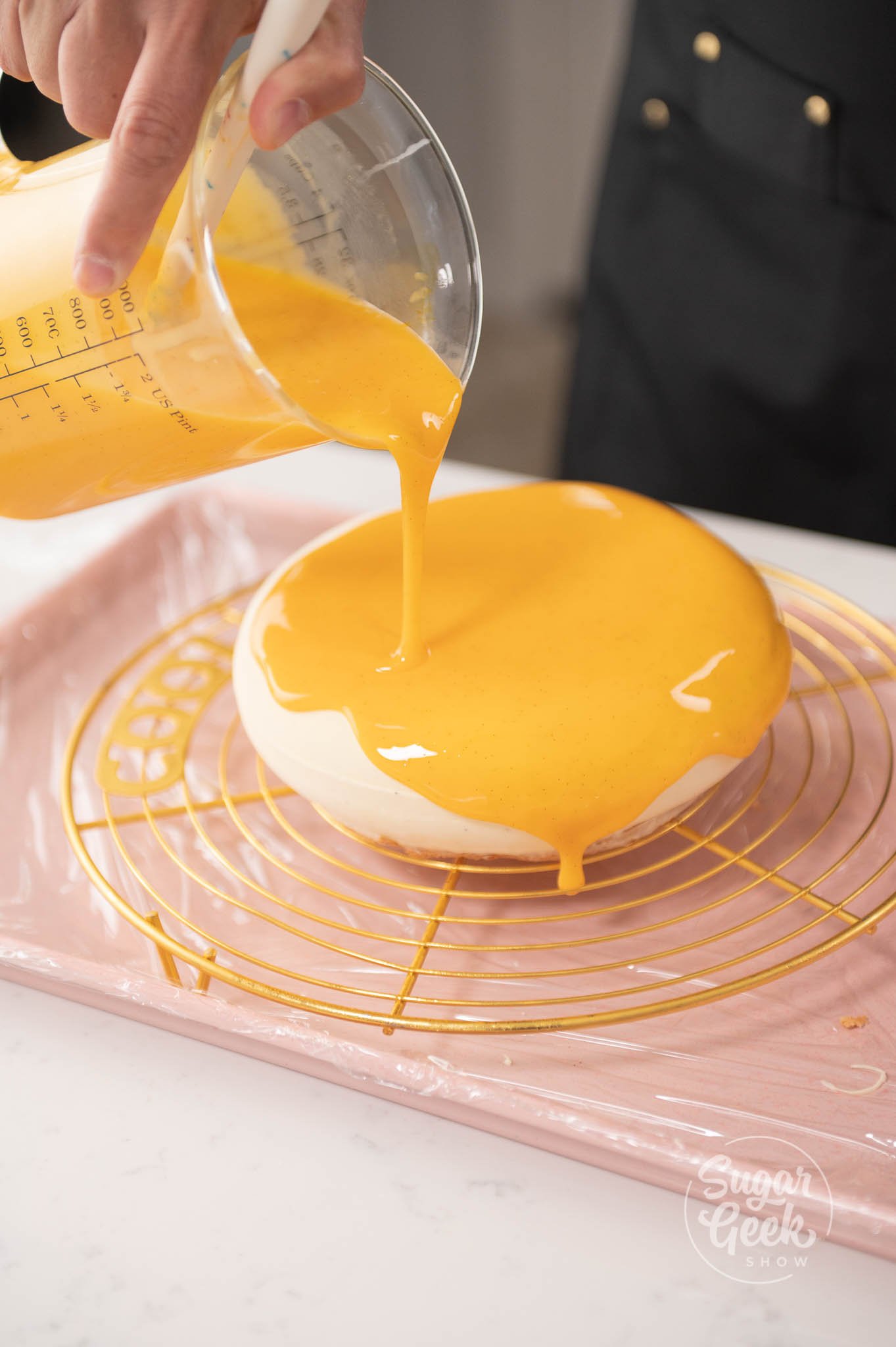 hand pouring measuring cup of glaze onto frozen entremet.