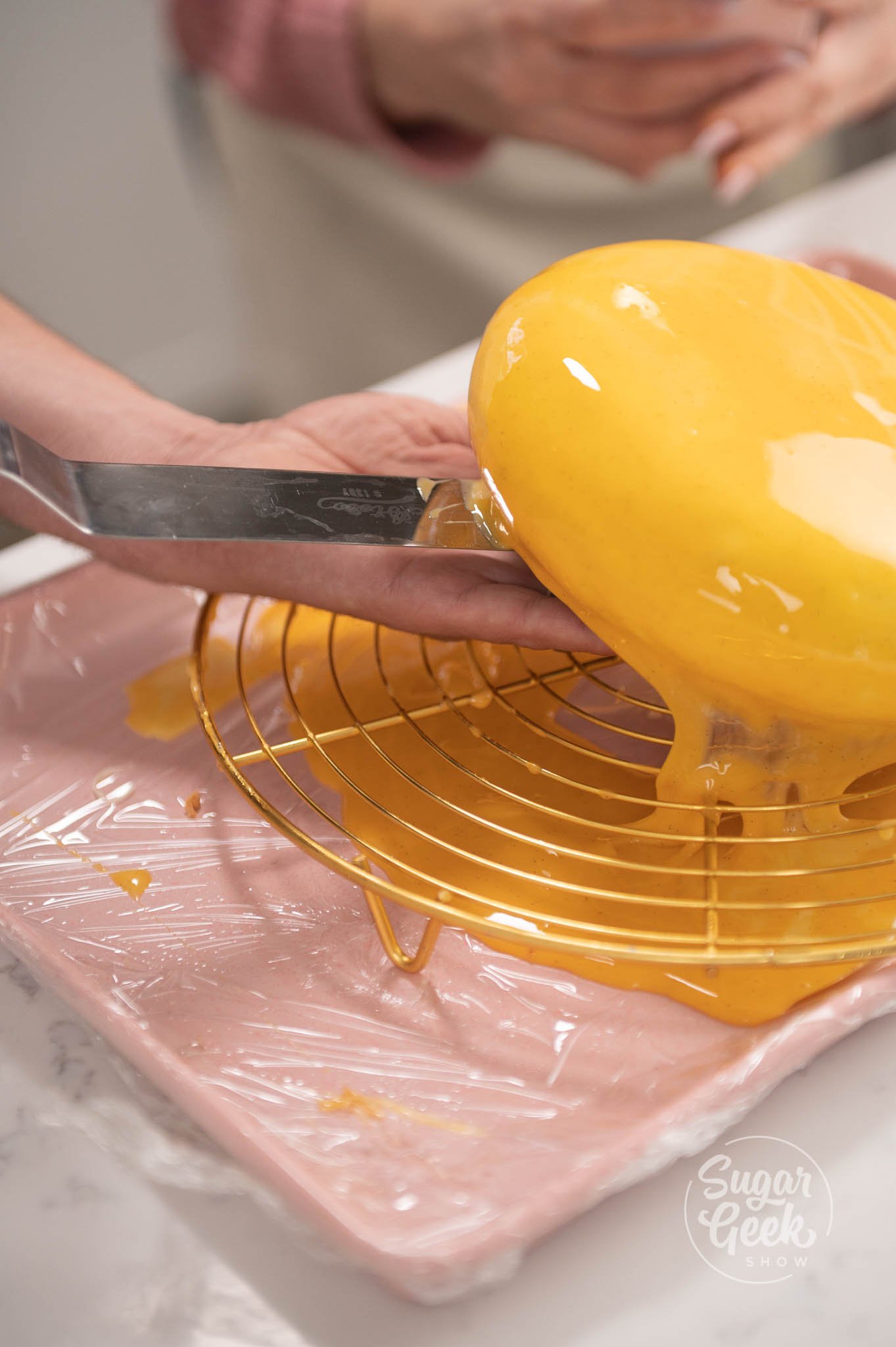 hand using spatula to remove entremet from cooling rack.