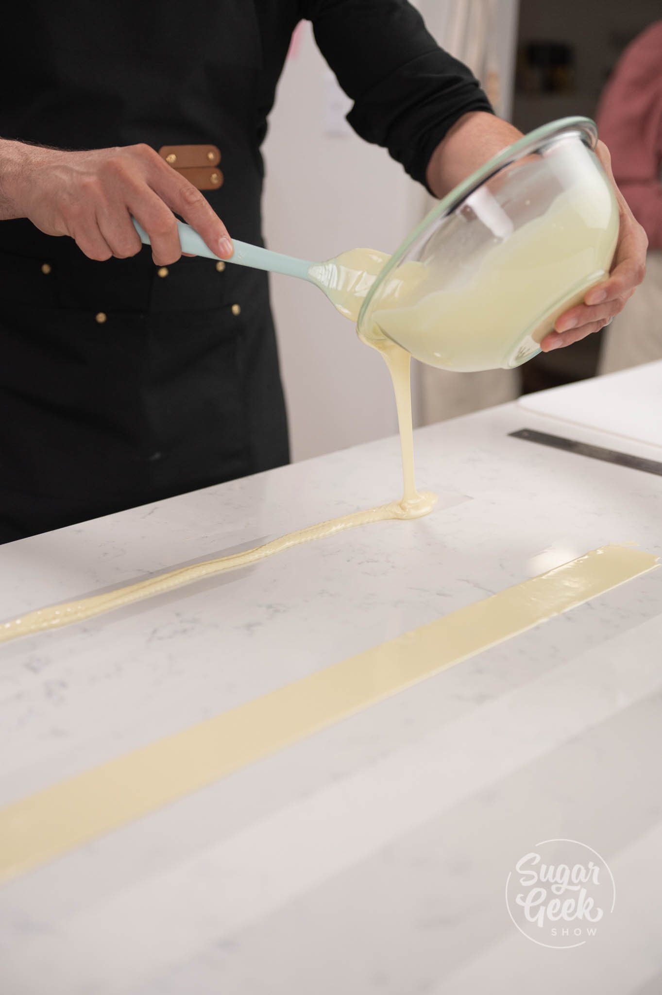 hand pouring bowl of white chocolate onto acetate sheets.
