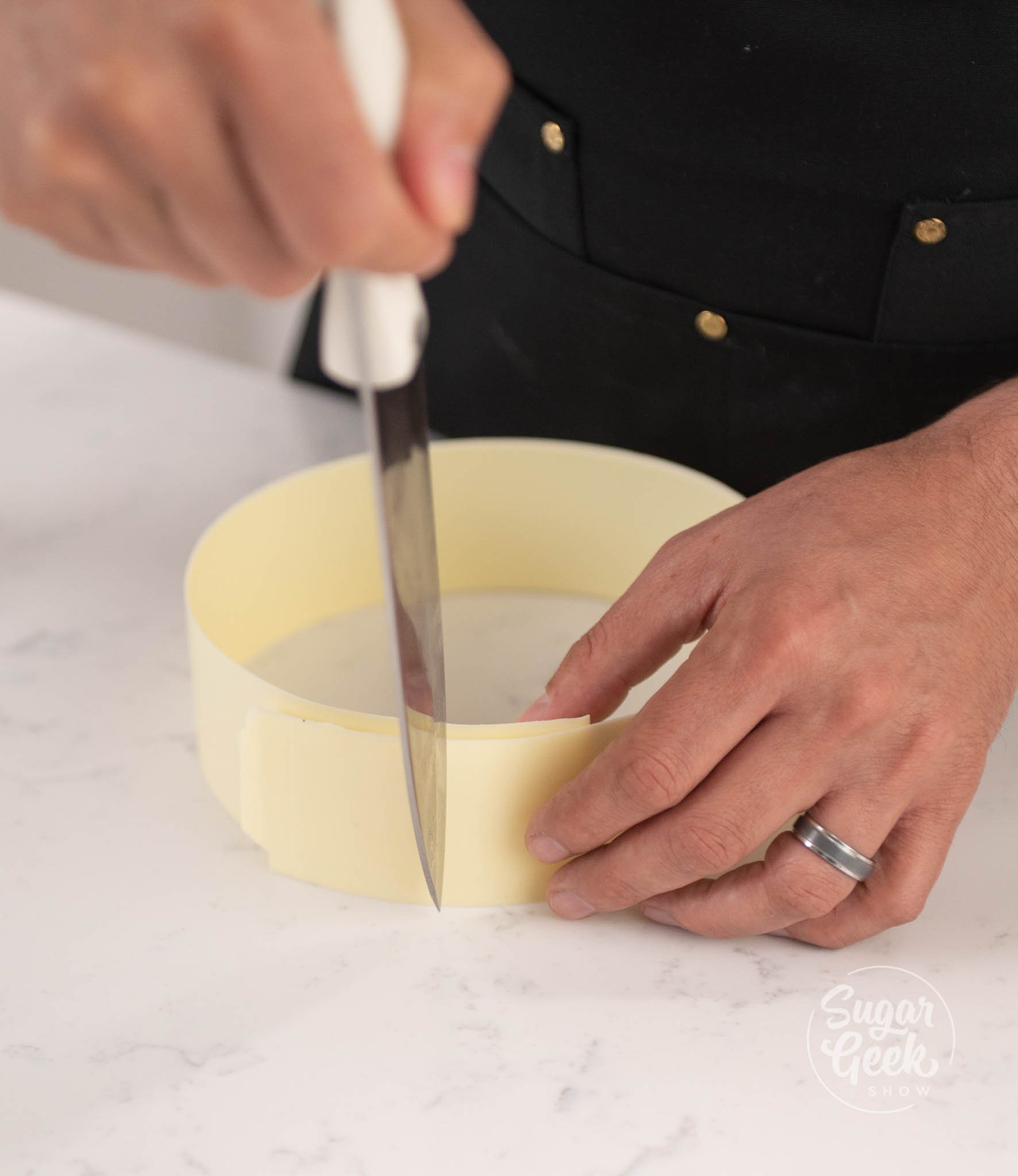 hands using knife to cut chocolate ring.
