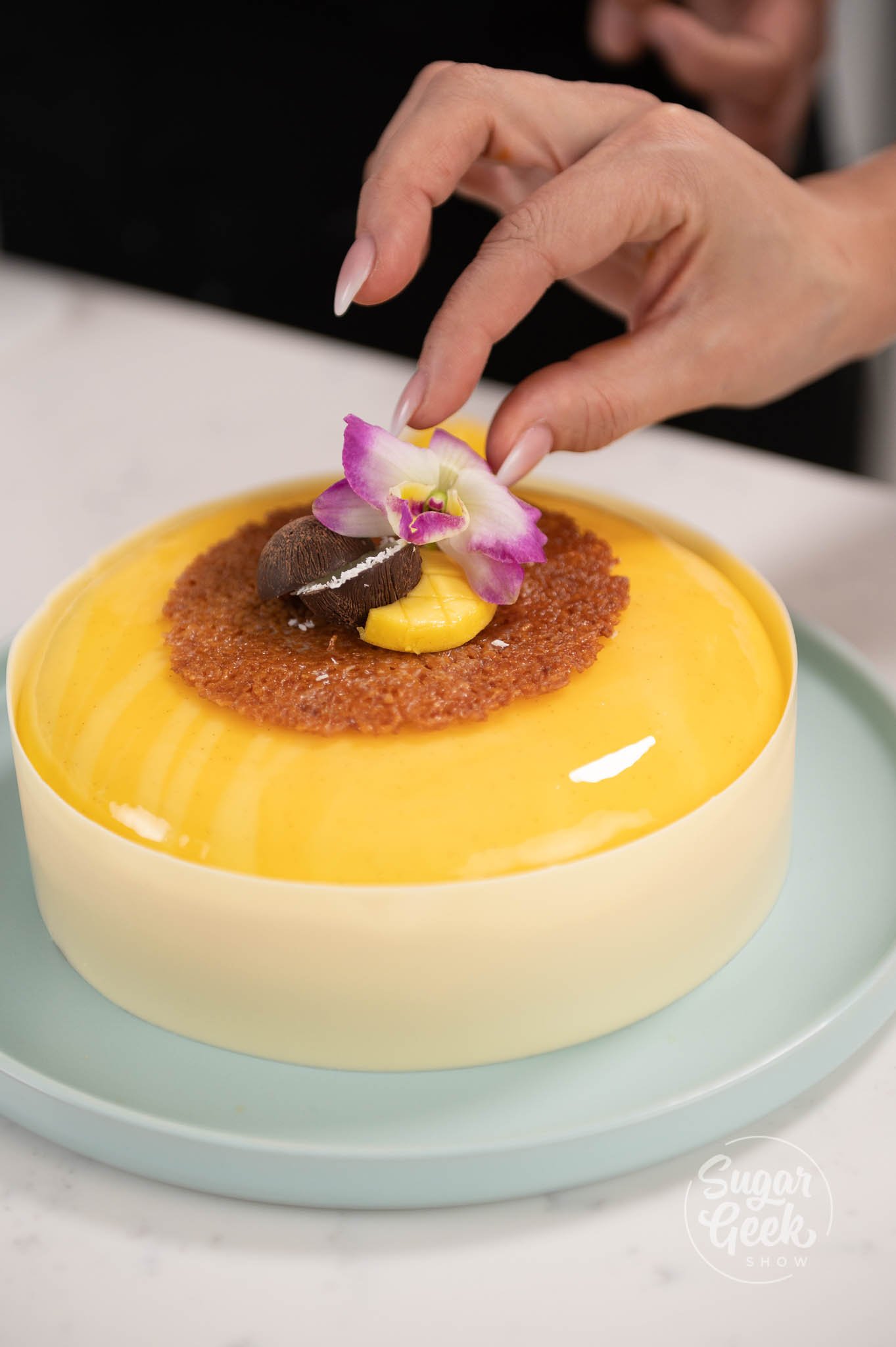 hand placing flower on top of decorated entremet.