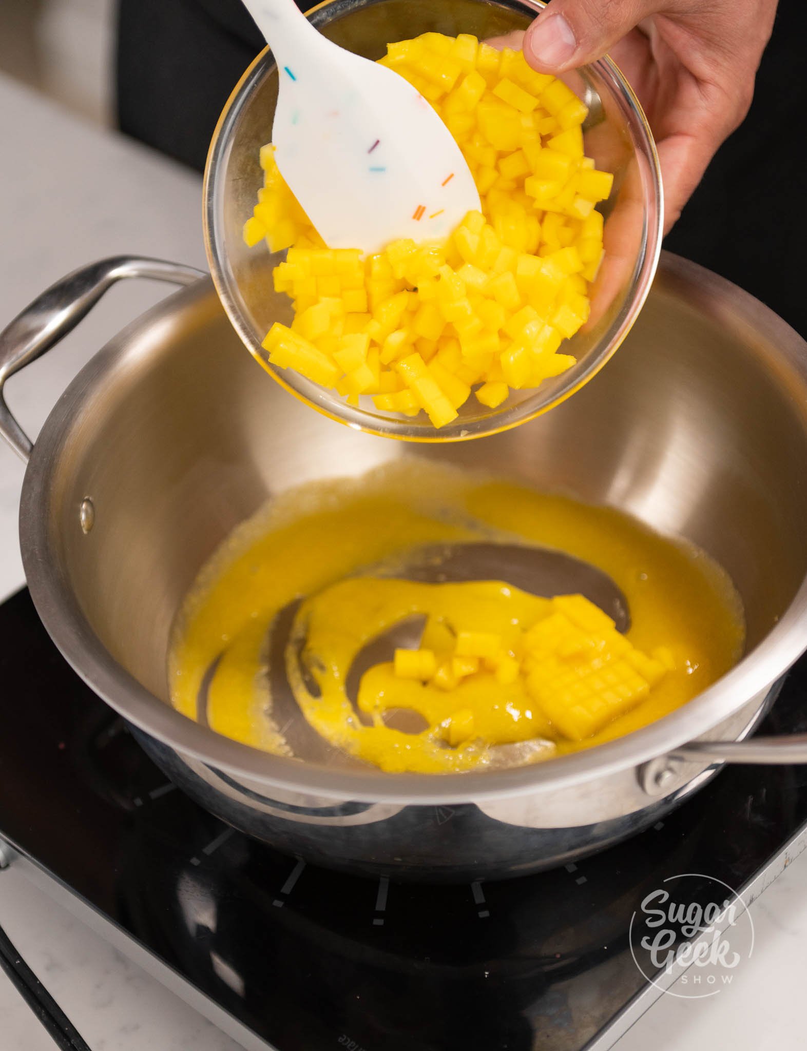 spatula inside bowl of diced mangos above saucepan.