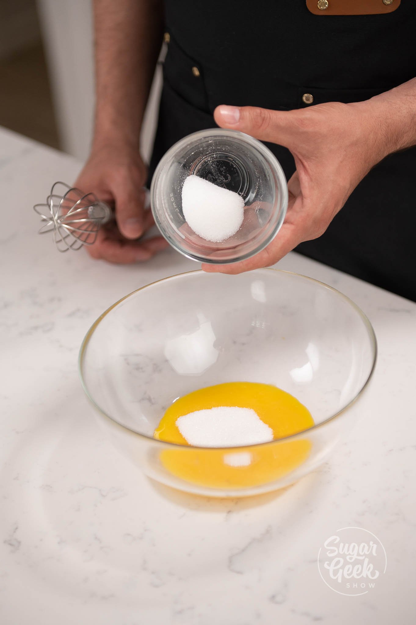 bowl of sugar being added to bowl of egg yolks