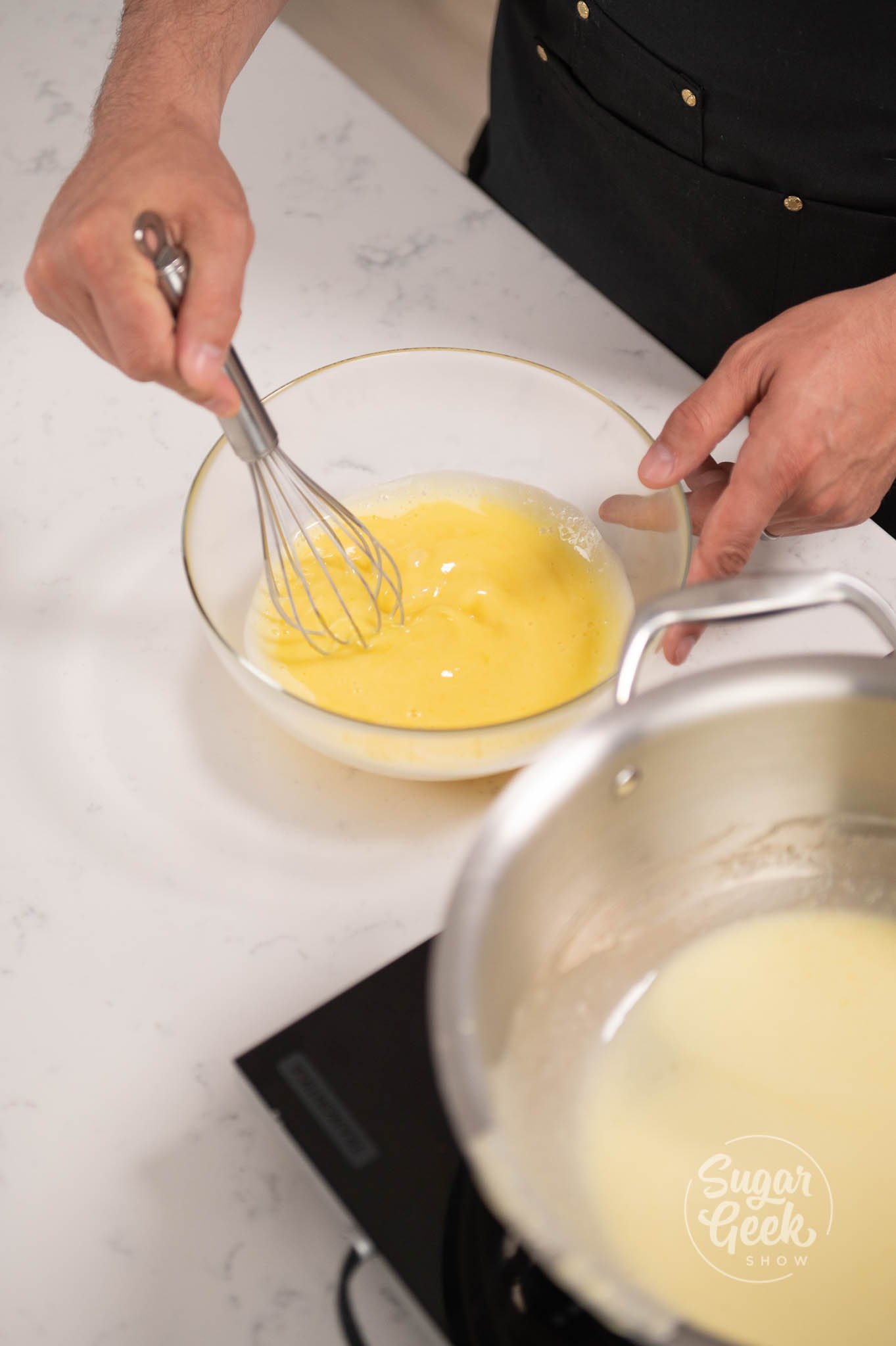 hand whisking bowl of yolks with a hand whisk.