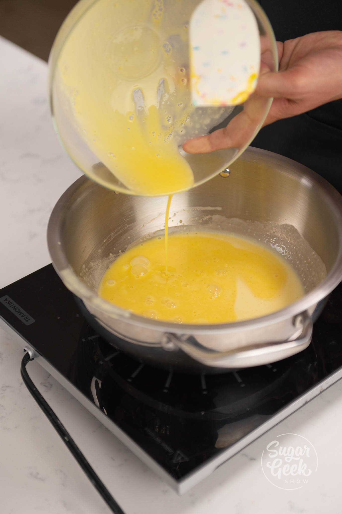 hand pouring tempered egg yolks back into pan