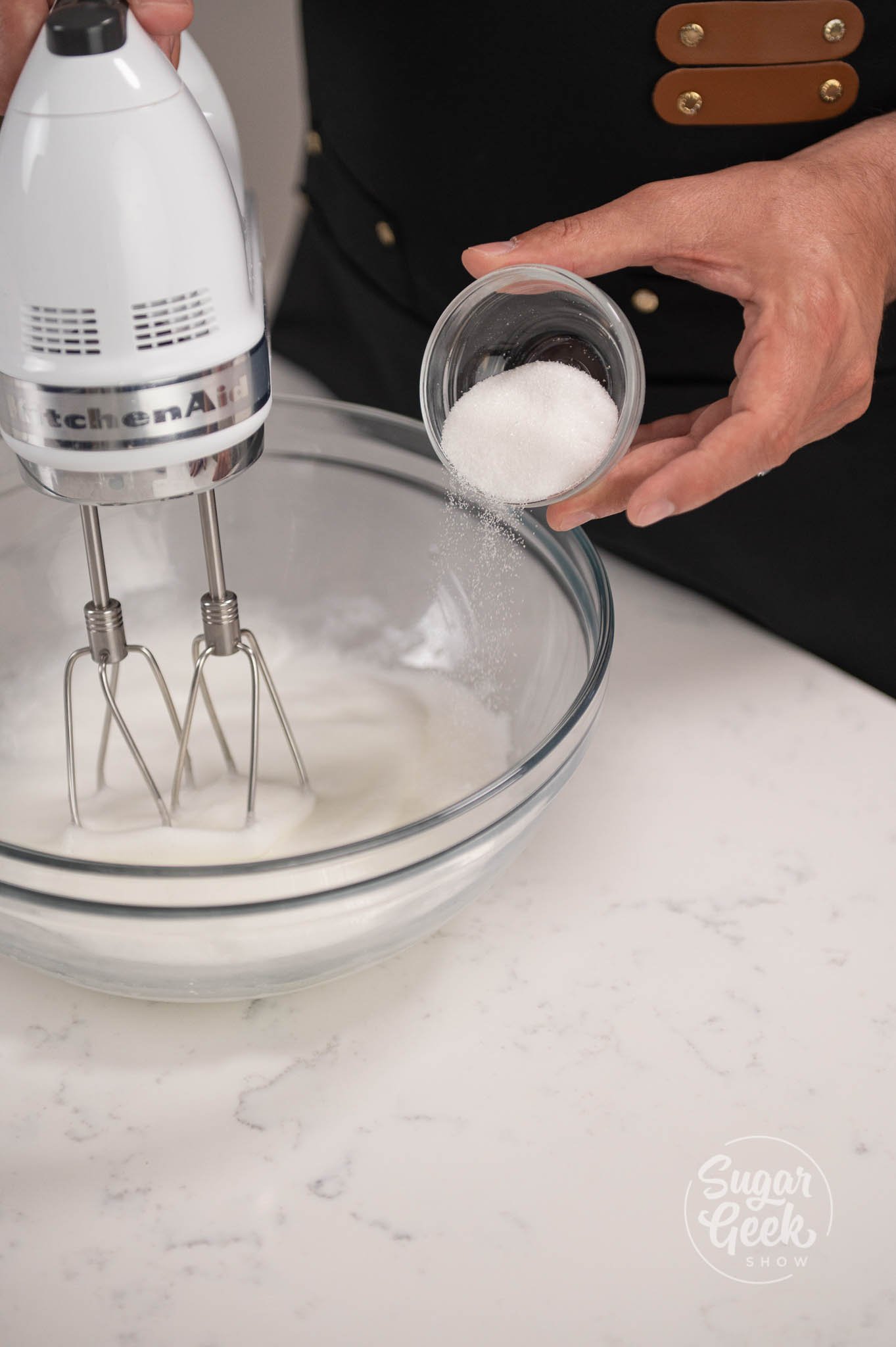 hand placing bowl of sugar into egg white mix.
