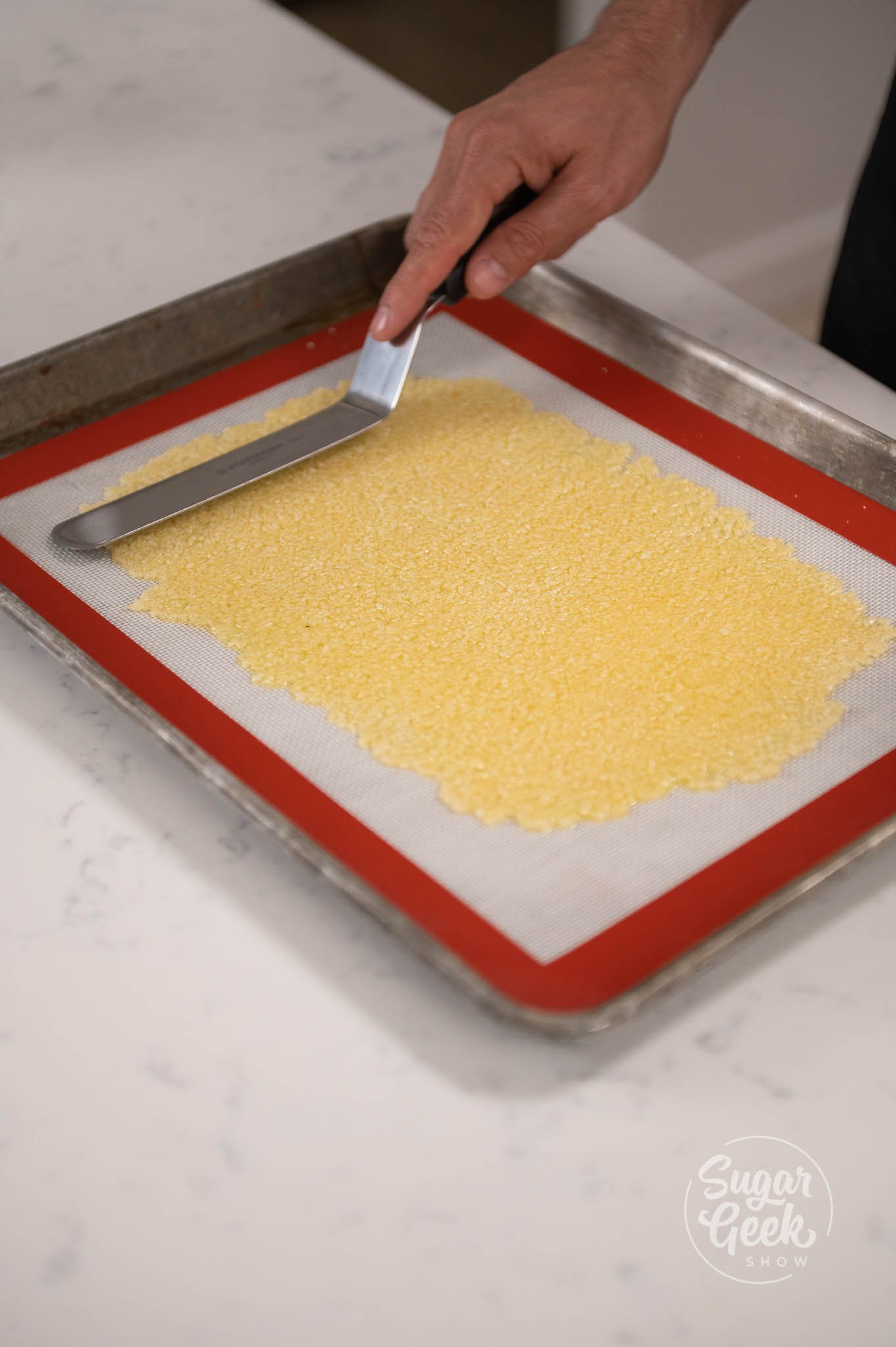 hand using spatula to spread nougatine on tray.