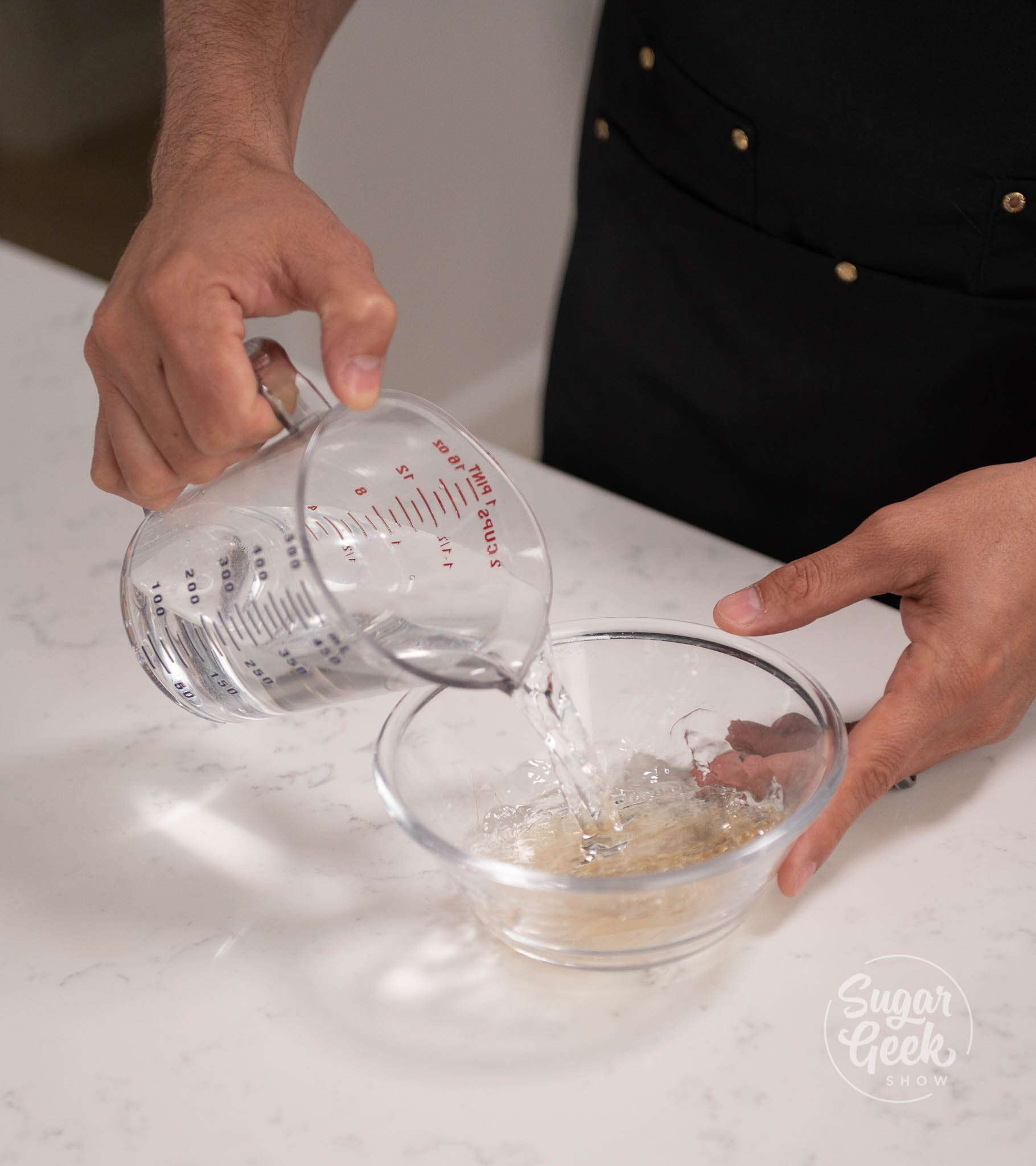 hand pouring measuring cup of water onto gelatin.