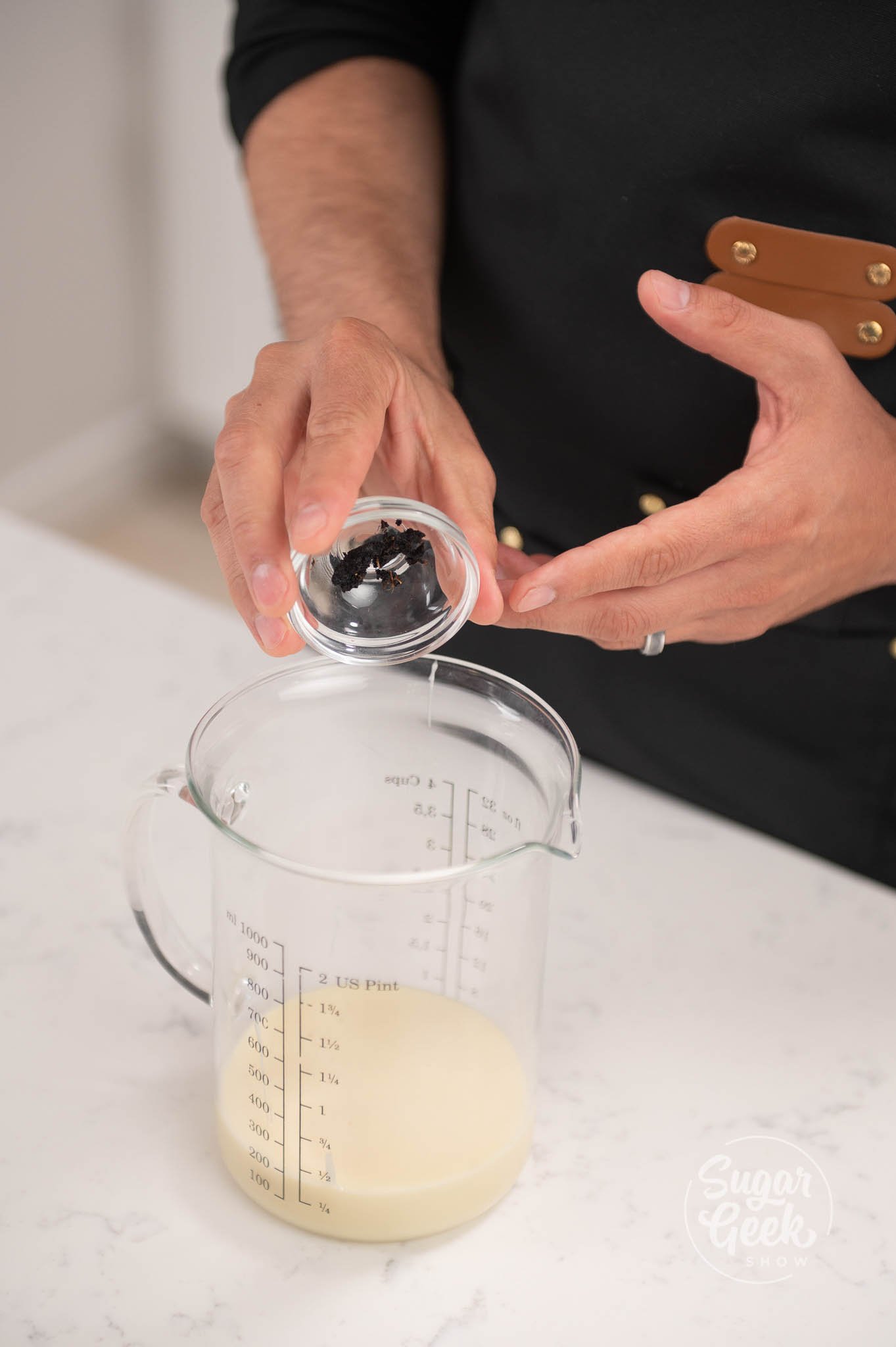 hand pouring conainer of vanilla into measuring cup.