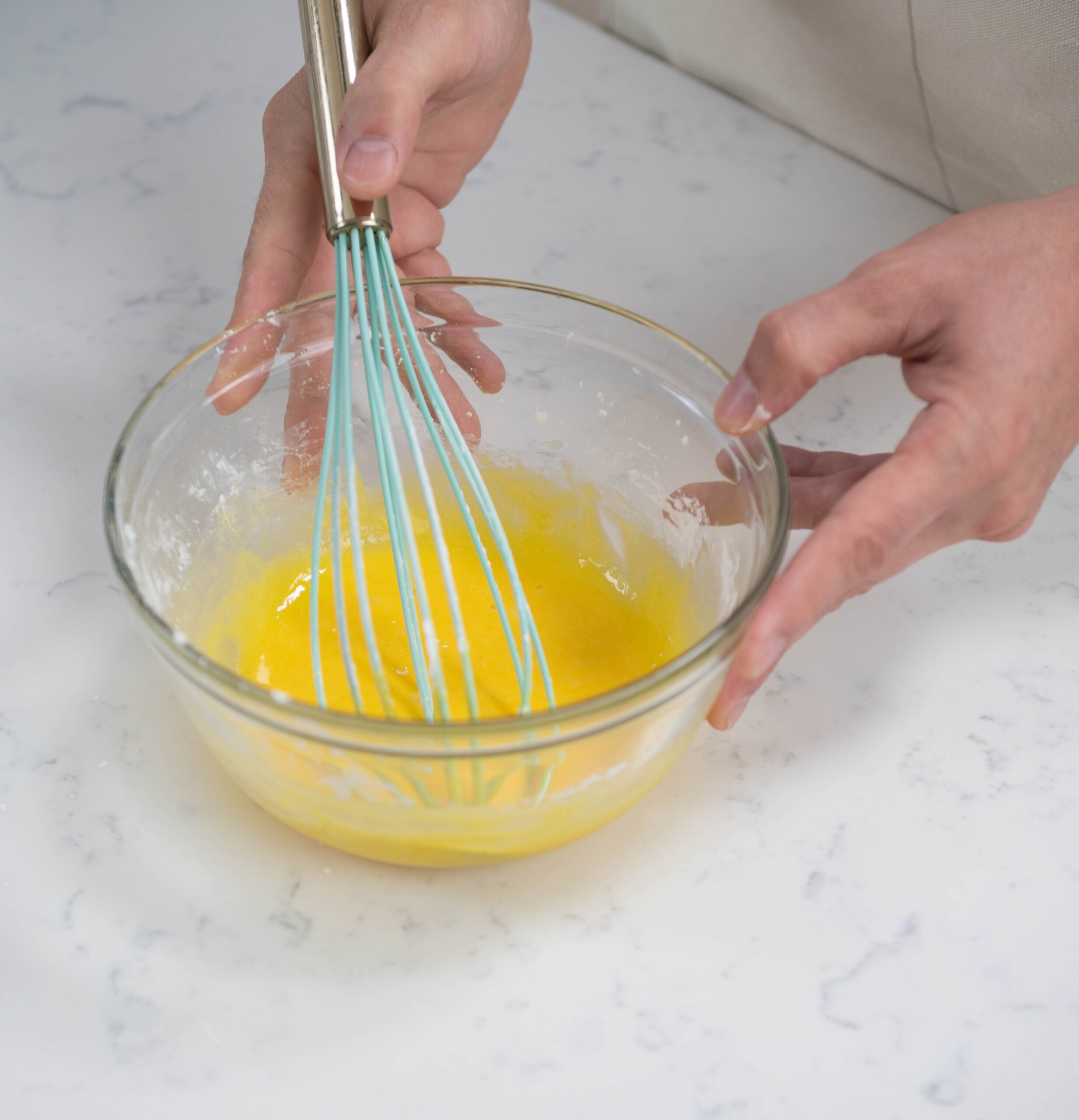 hands holding bowl of egg yolks with whisk