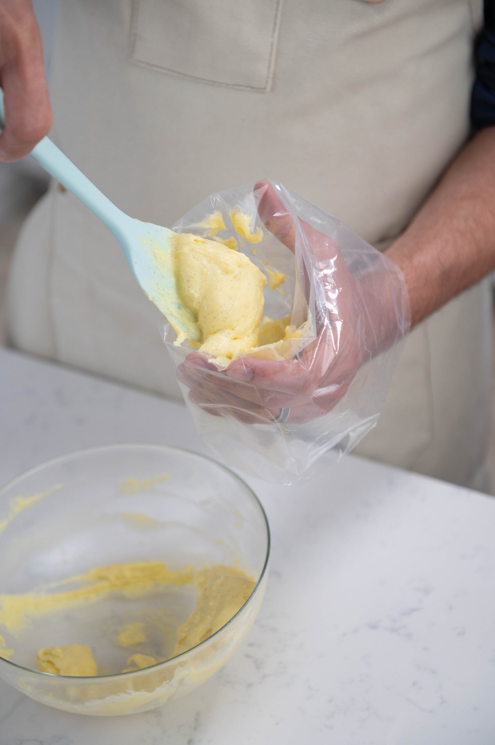Hand using spatula to fill piping bag with pastry cream.