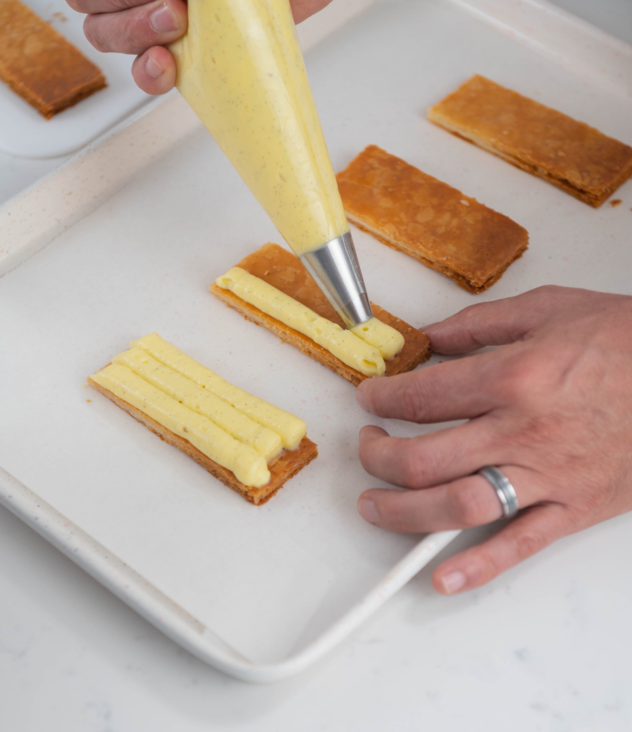 hand using piping bag to pipe pastry cream onto puff pastry.