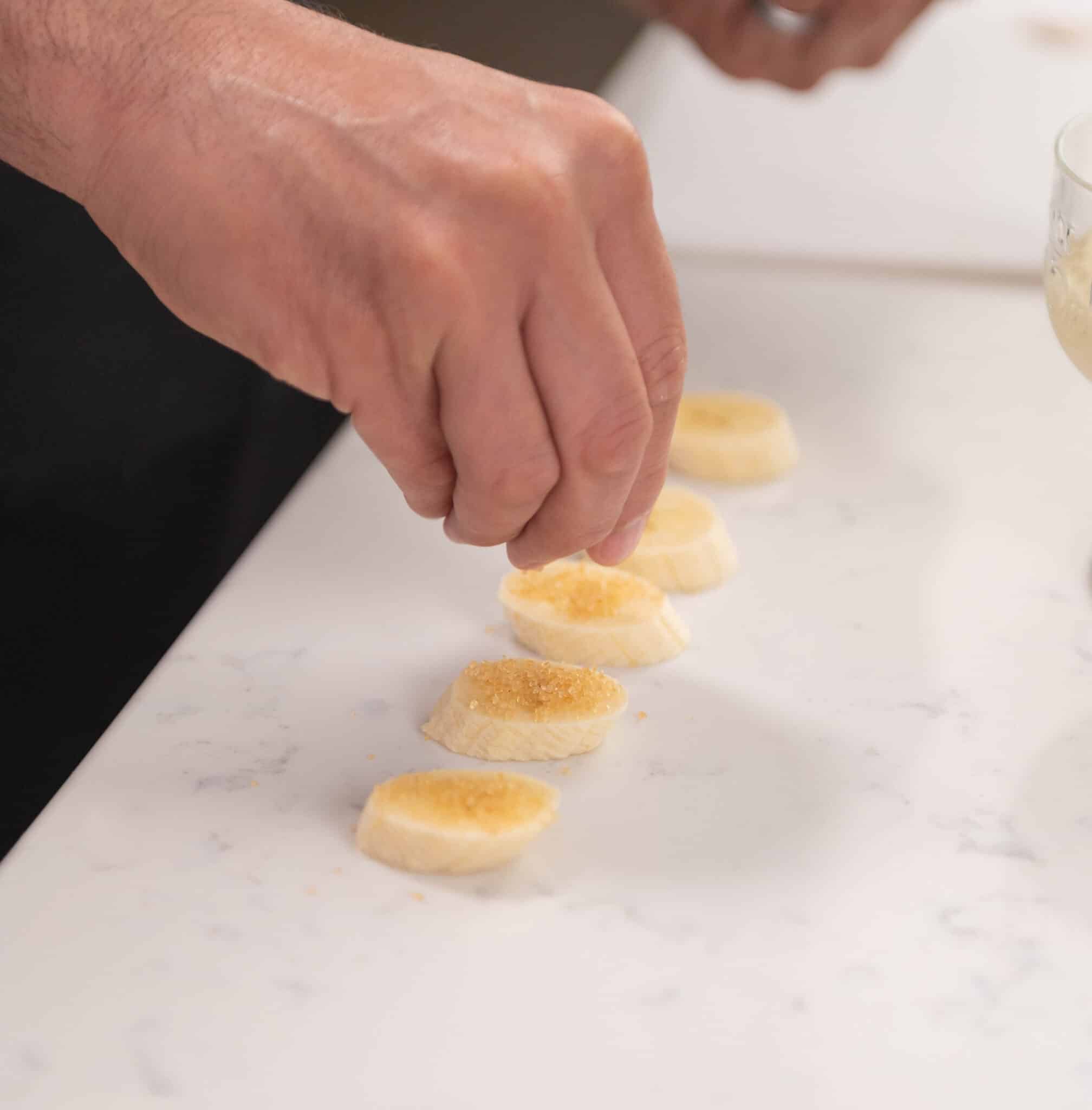 hand adding sugar in the raw on top of banana slices.