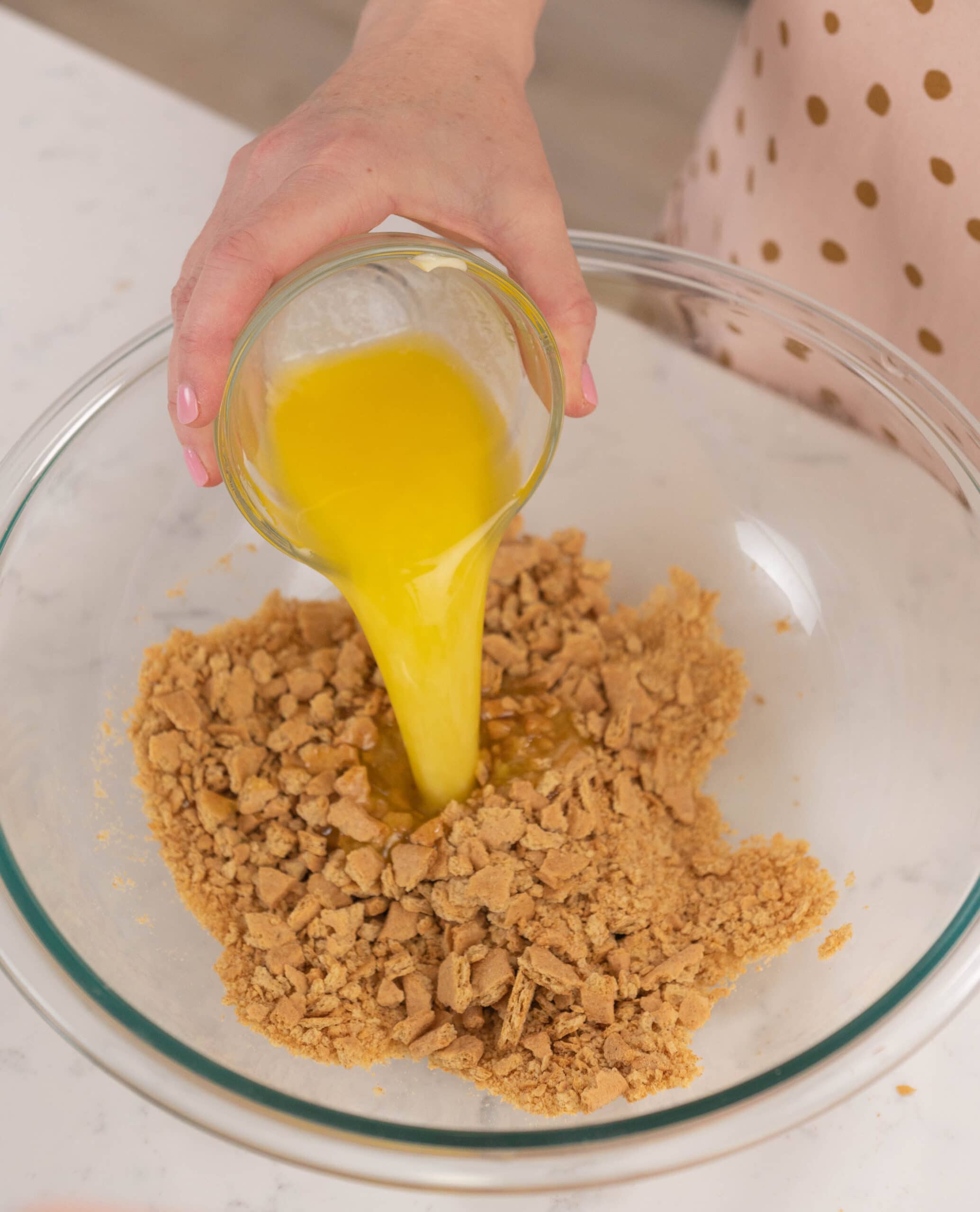 hand pouring bowl of melted butter into graham cracker crust.