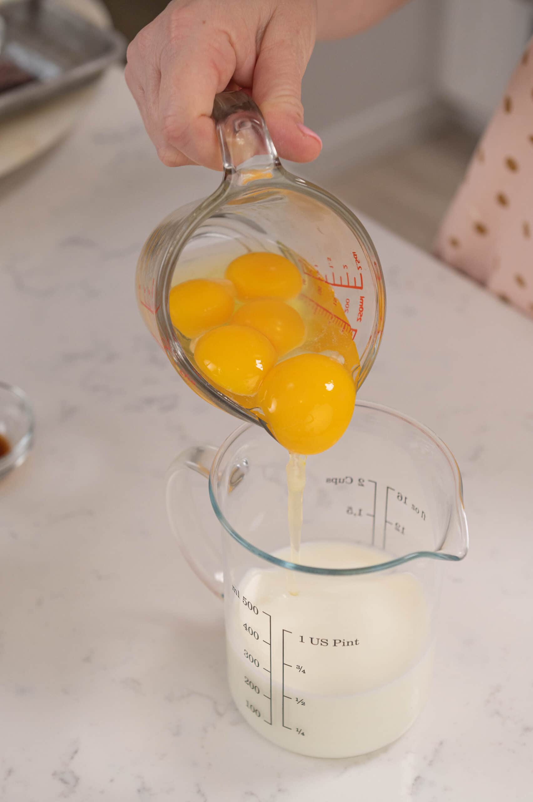 hand pouring measuring cup filled with eggs into measuring cup filled with buttermilk.