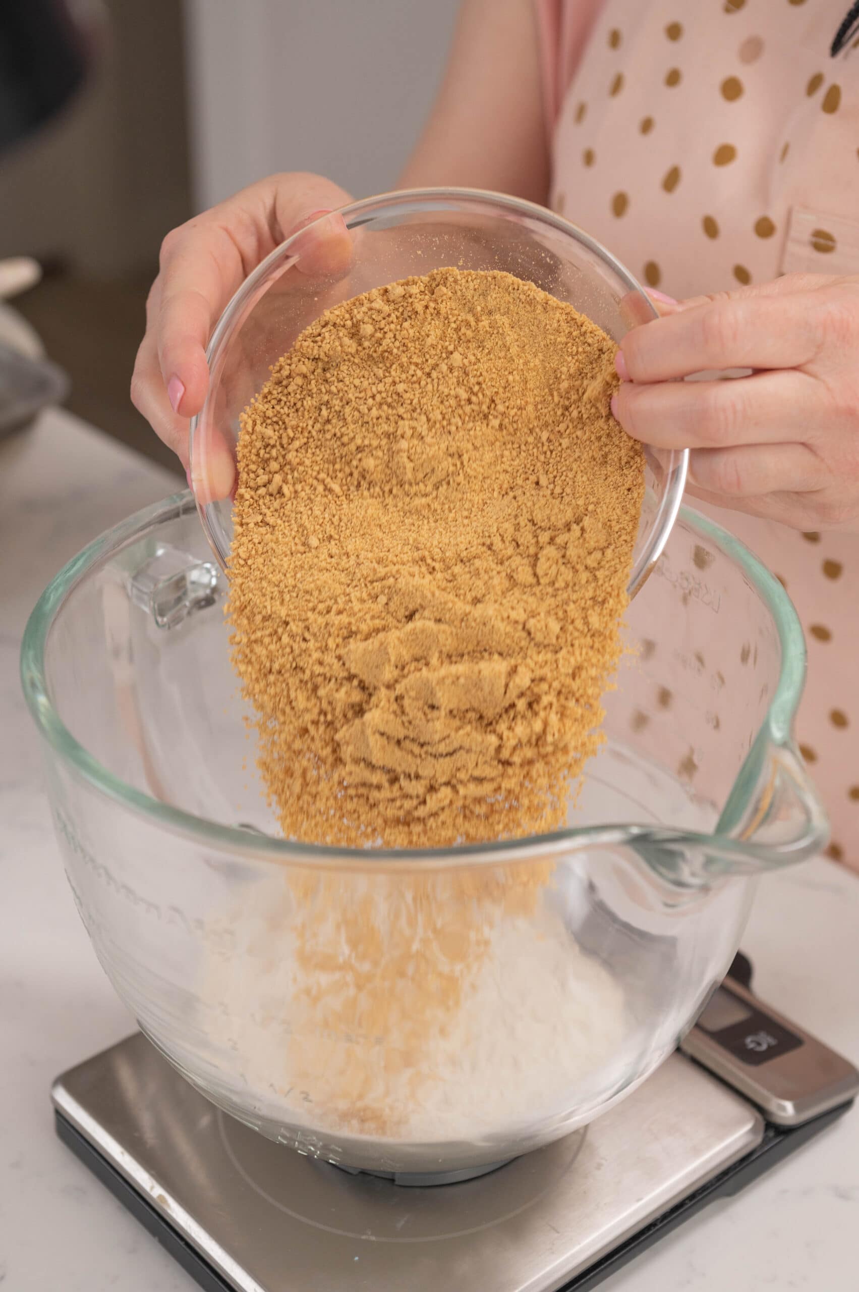 hand pouring bowl of graham crackers into stand mixer bowl.