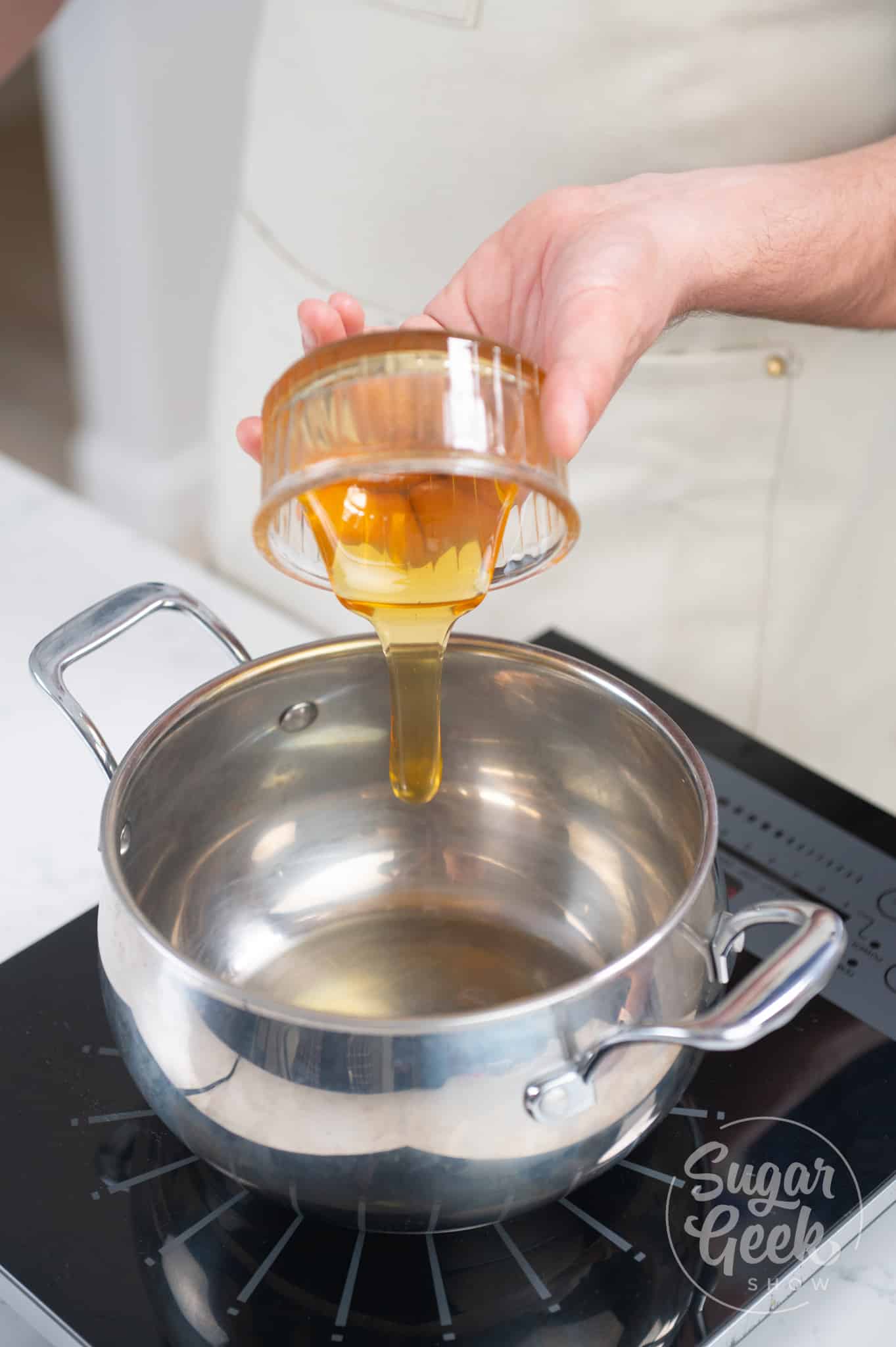 hand adding honey to saucepan.