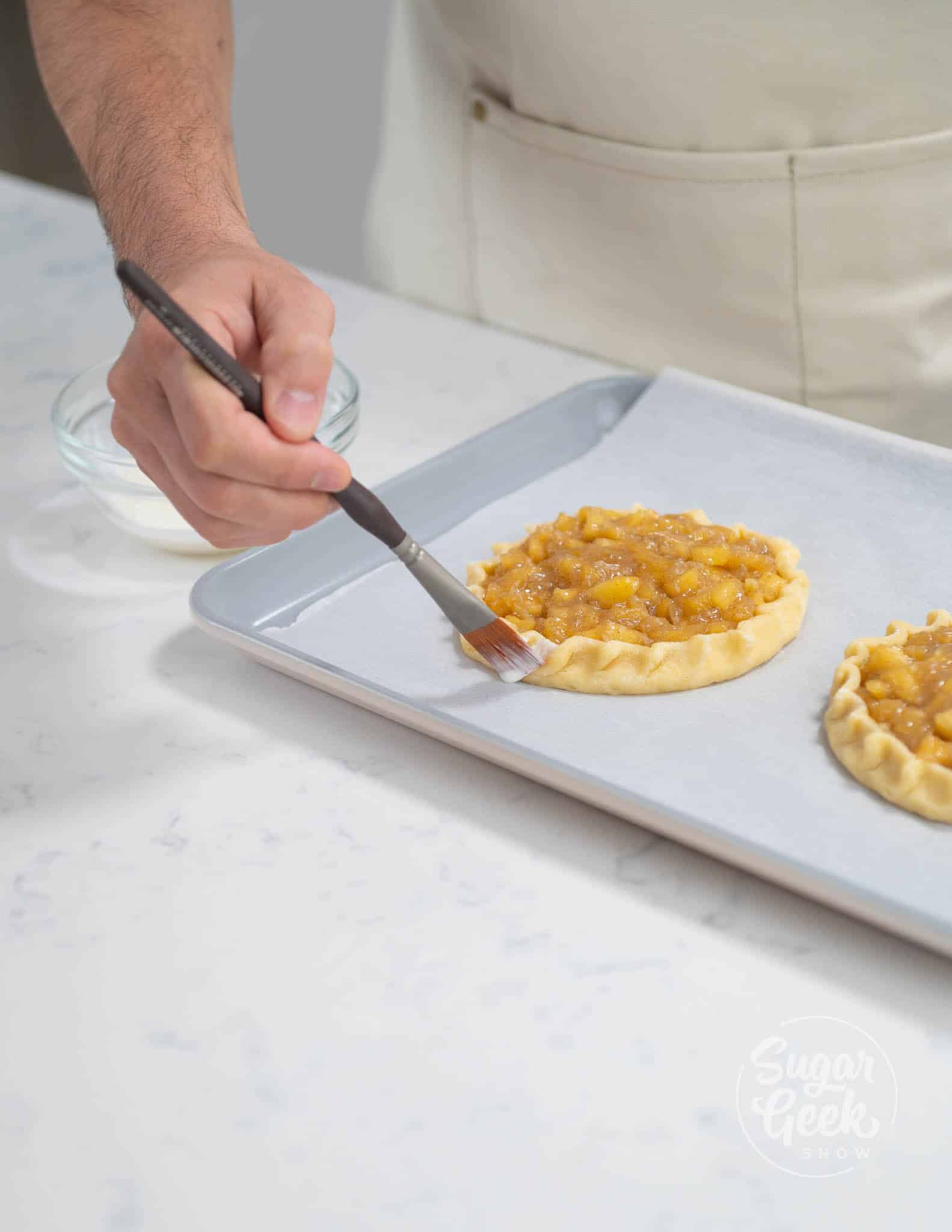 hands using brush to brush layer of cream on to dough
