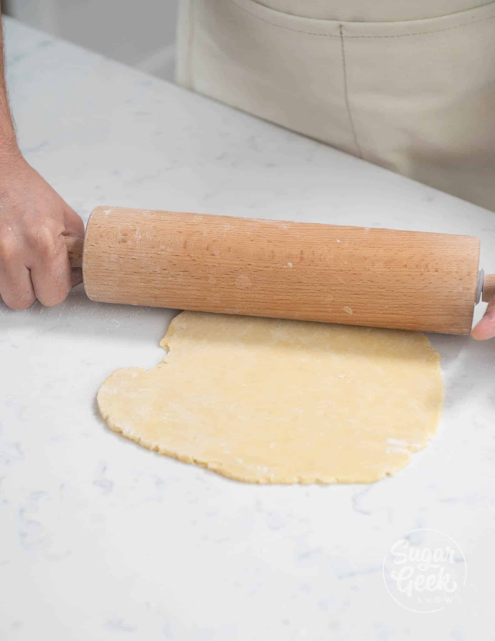 hands usiing rolling pin to roll out dough.