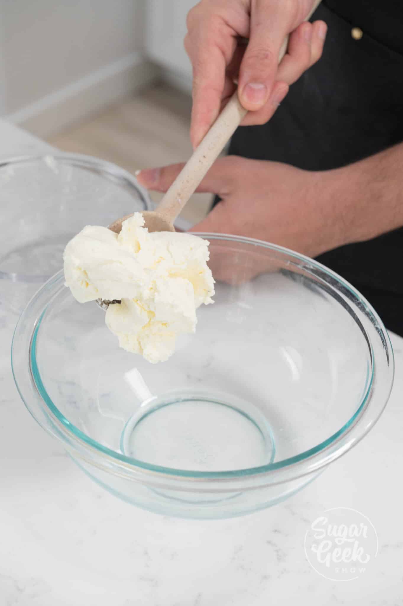 hand using spoon to spoon cream cheese into bowl.