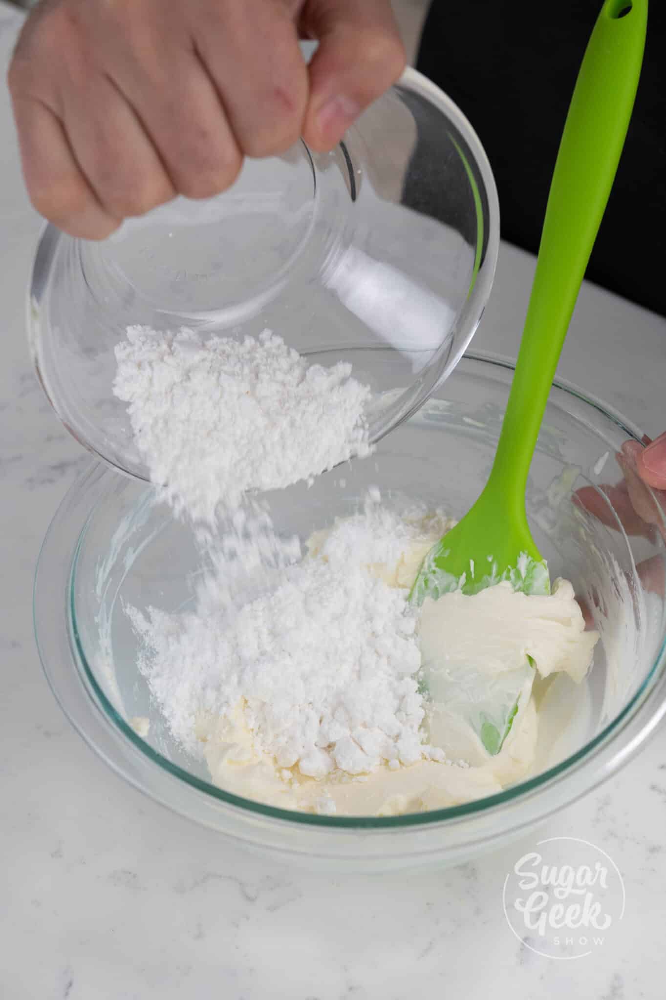 hand adding powdered sugar to cream cheese mix.