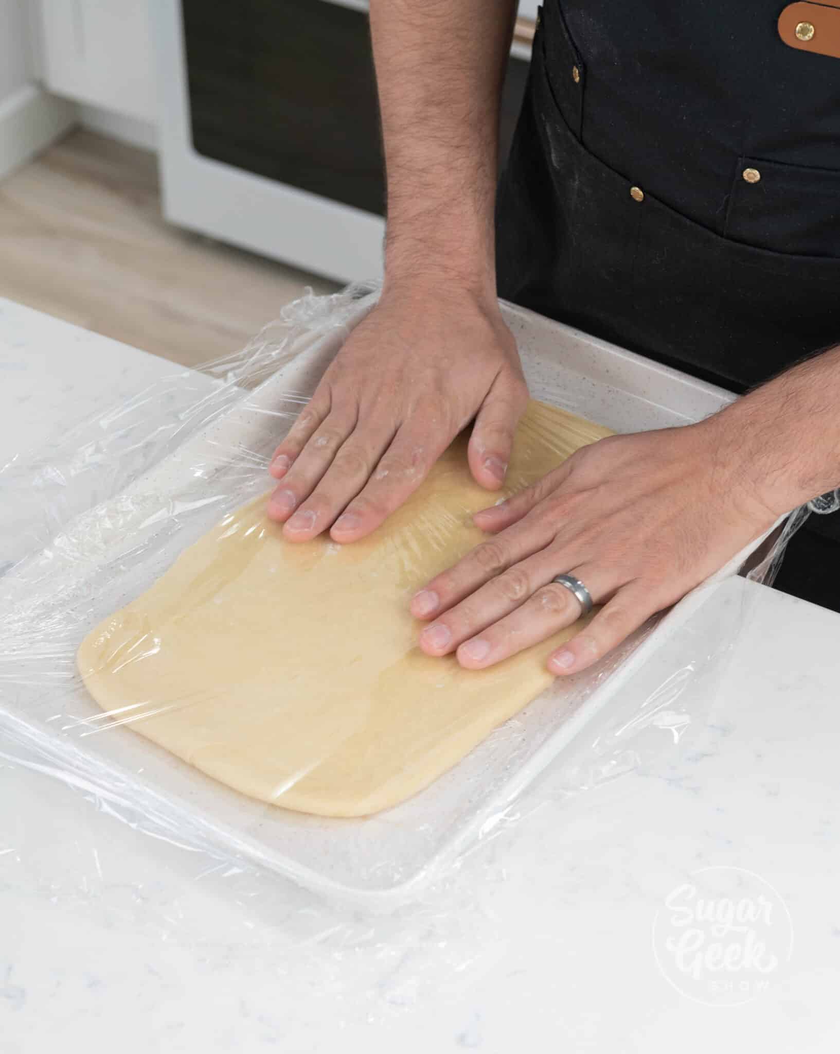 hands on top of covered and rolled out dough.