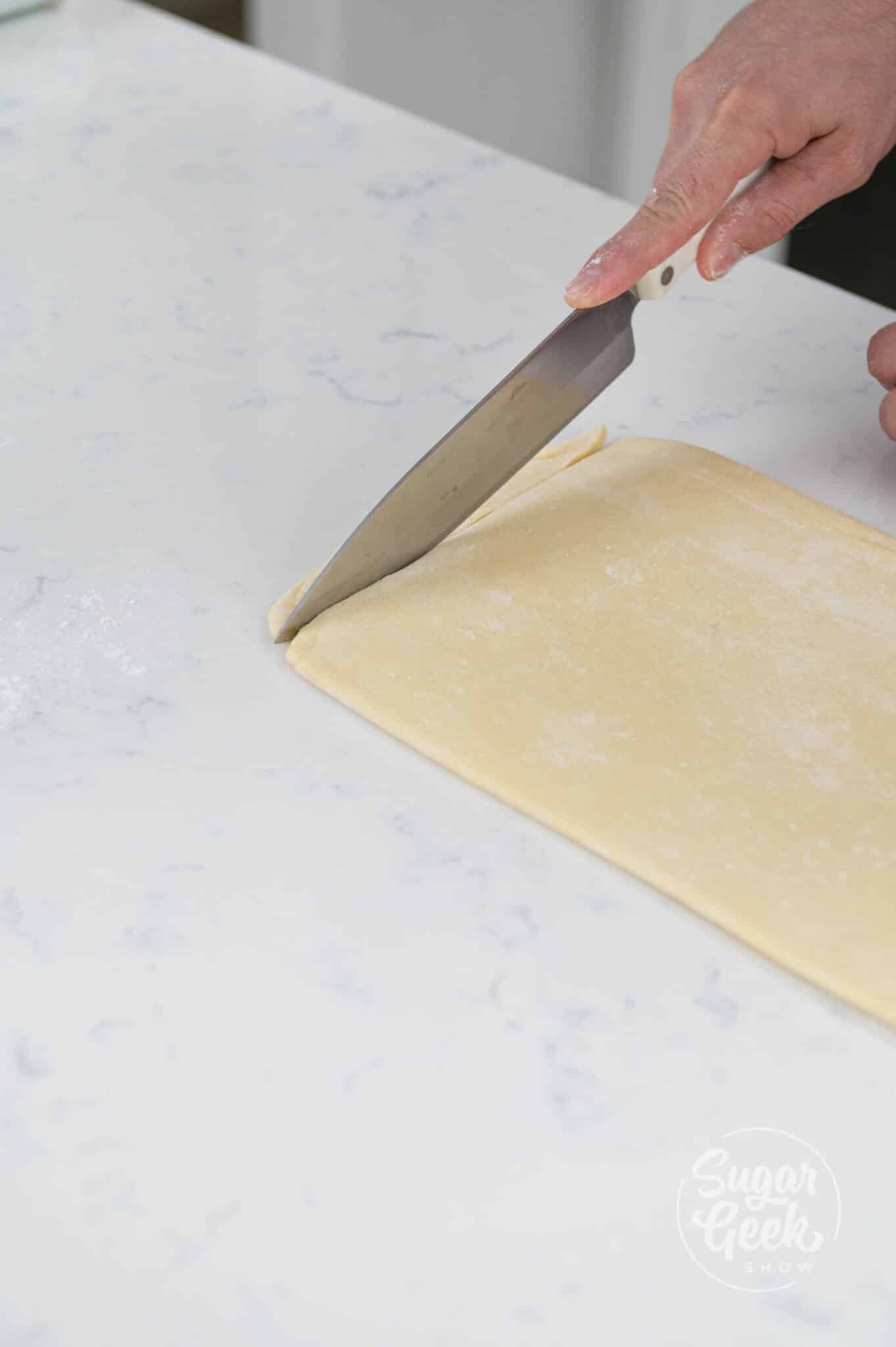 hands using knife to cut ends of the dough.