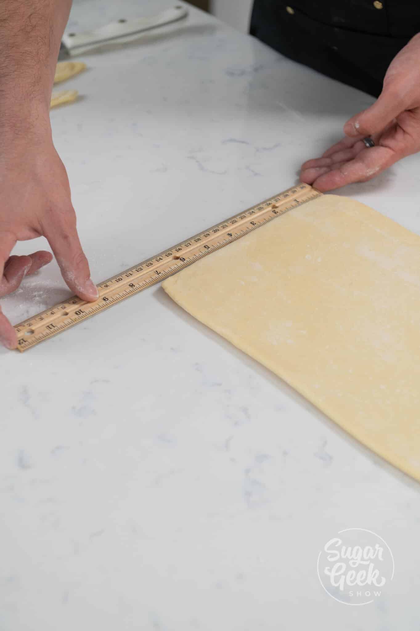 hand holding ruler next to dough.