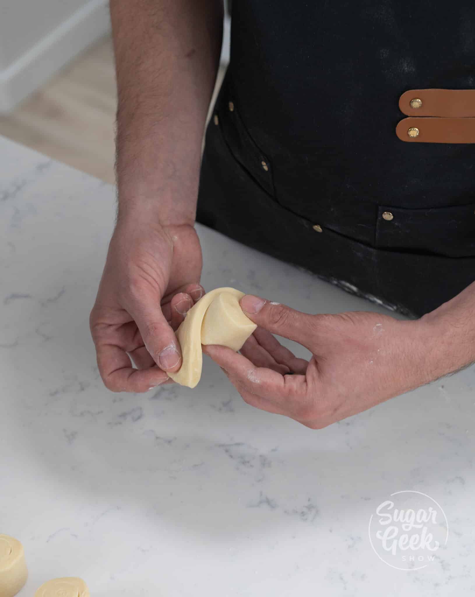 hands folding dough to create danish shape.