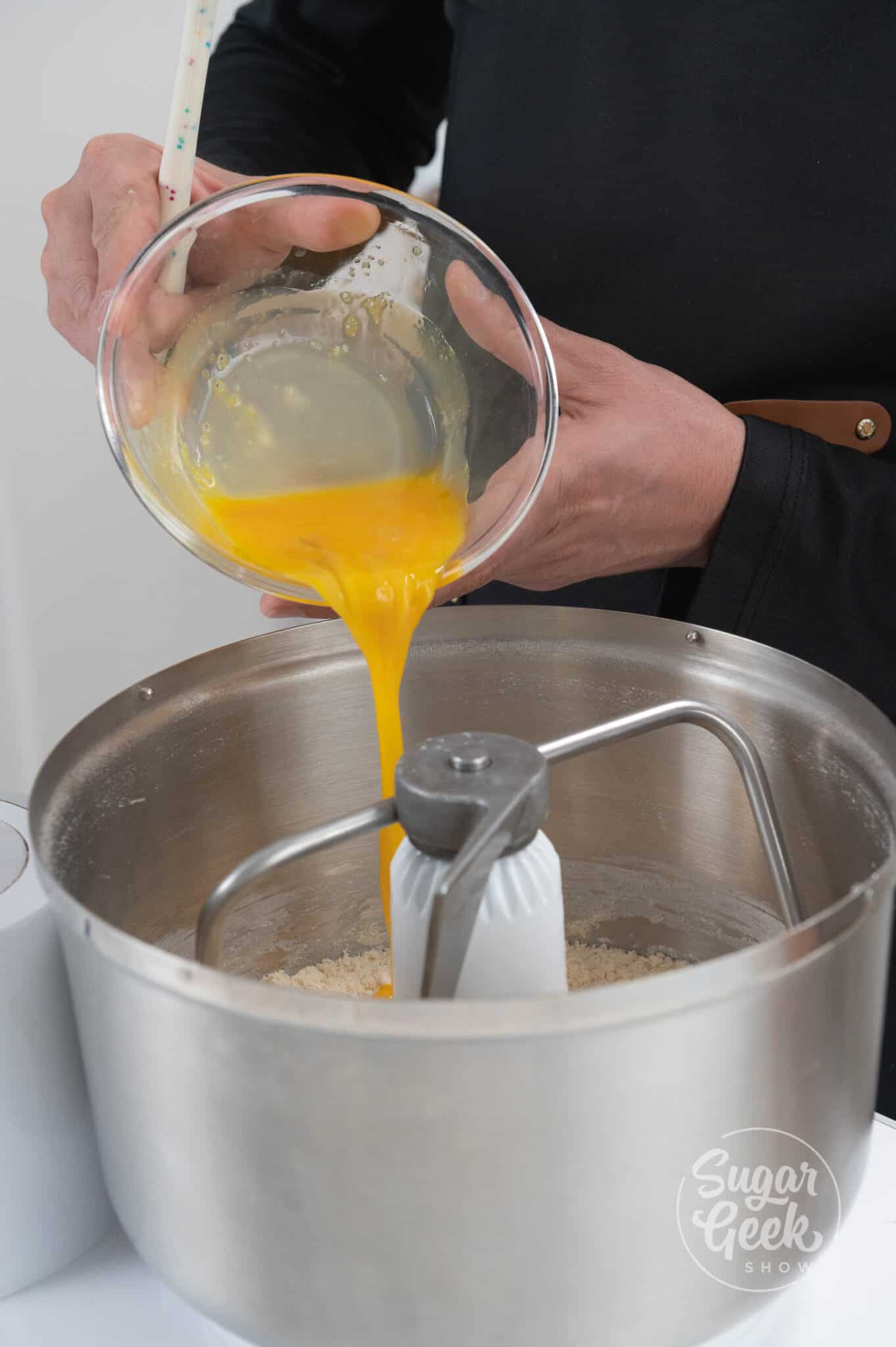 hand adding bowl of egg yolks into stand mixer