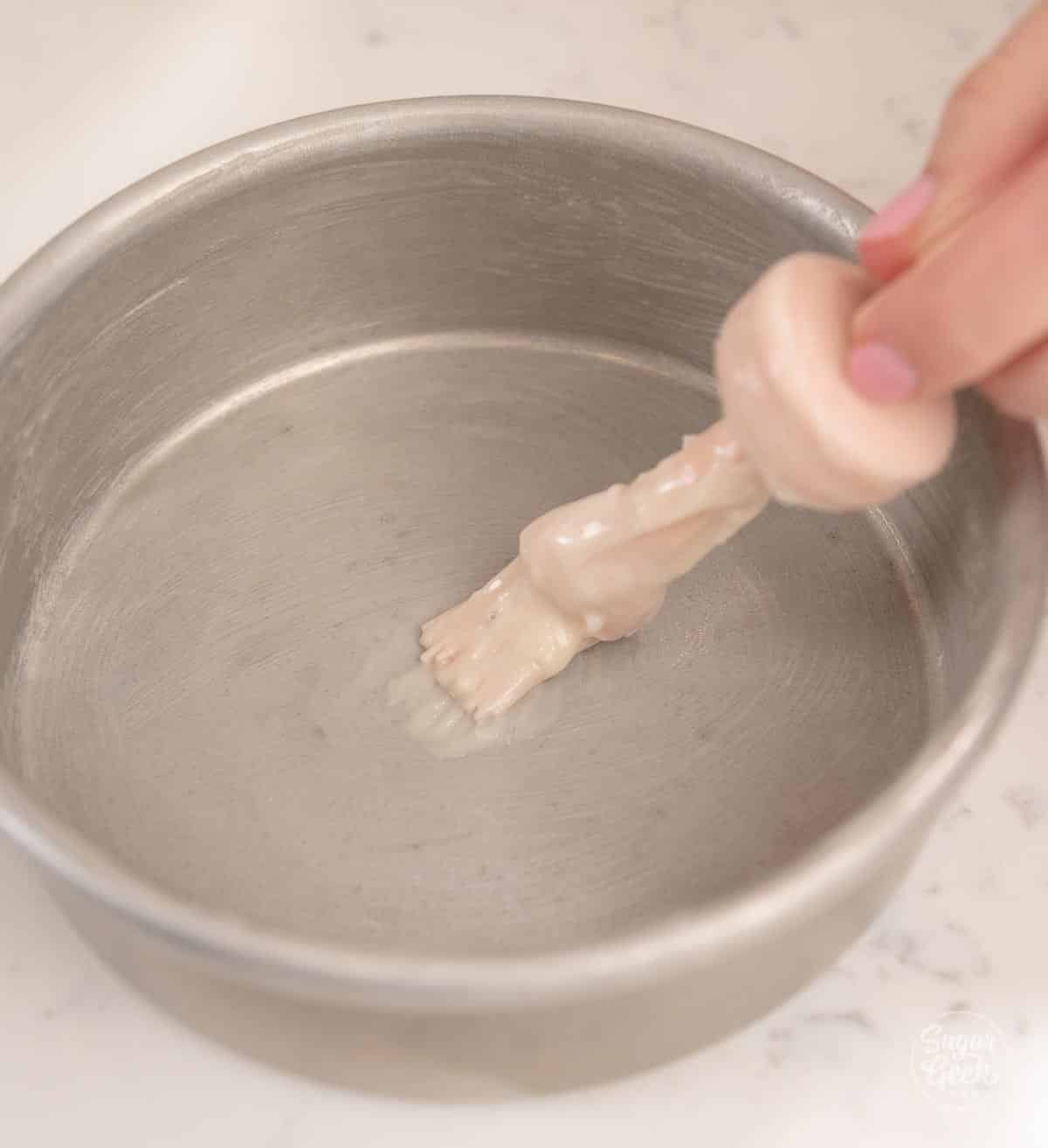 Silicone brush applying cake goop to a cake pan.