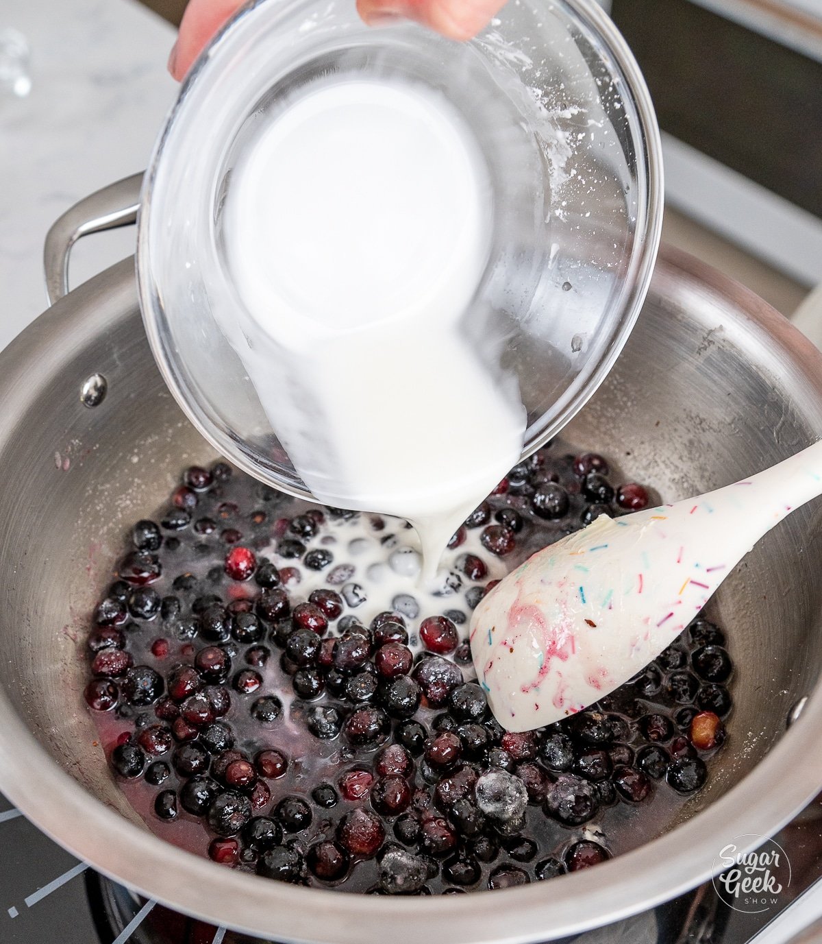 adding cornstarch slurry to cooking blueberries and stirring with a spatula.