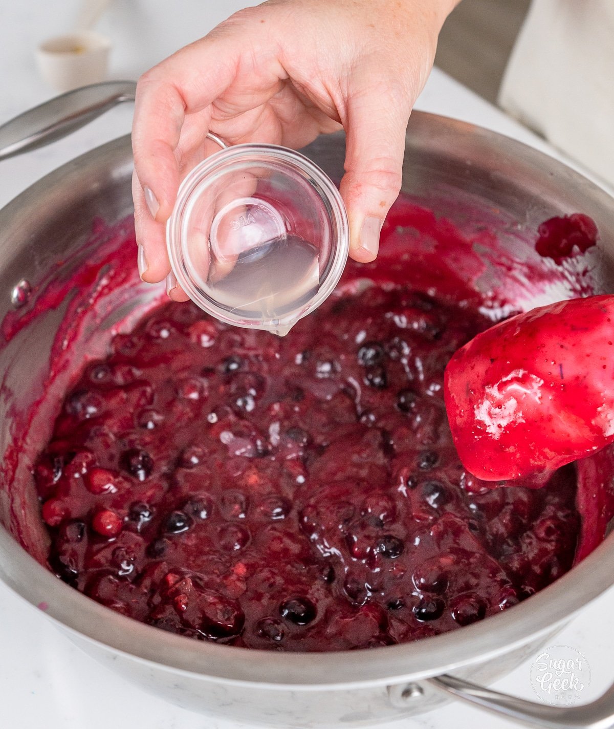hand adding lemon juice to cooking blueberry pie filling.