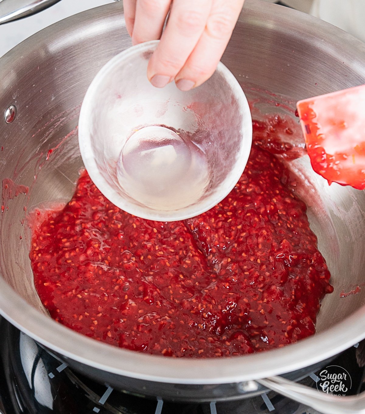 hand pouring lemon juice into raspberry mixture in a pot.