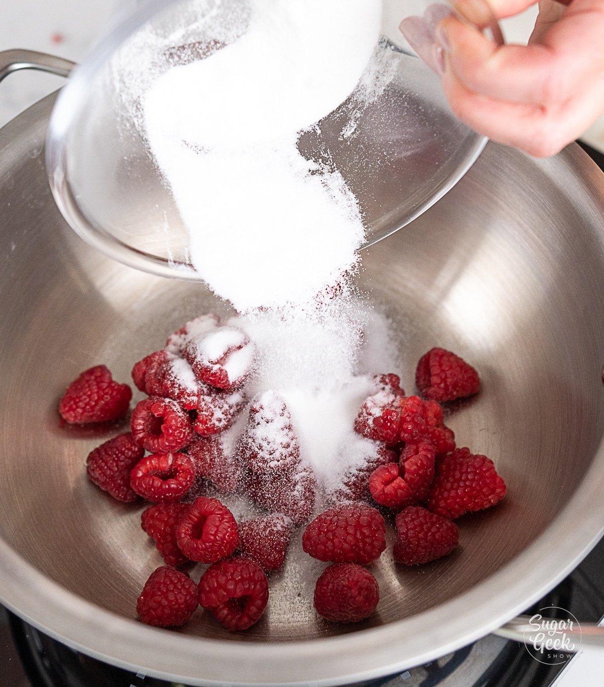 hand pouring sugar onto raspberries in a pot.