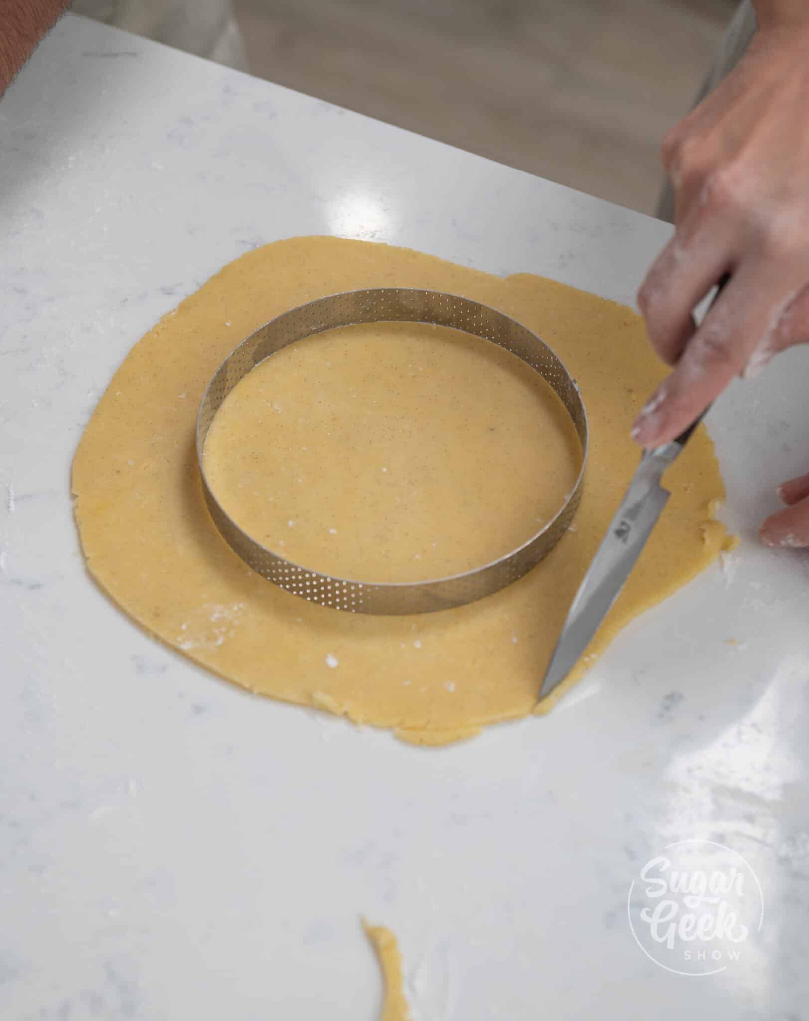 hand using knife to cut circular shape out of tart dough.