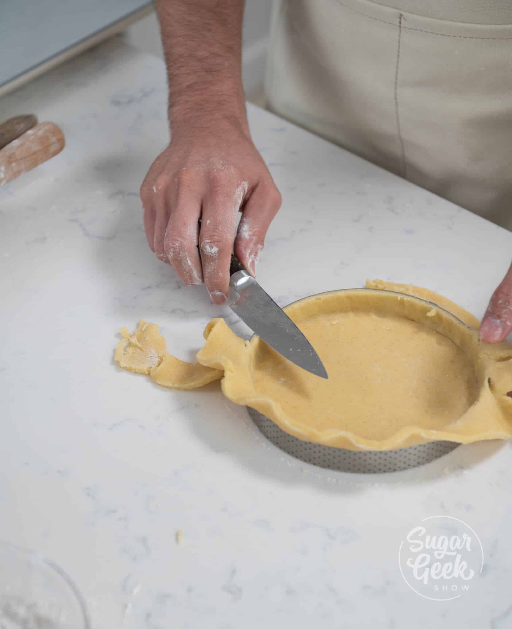hand using knife to cut excess off the top of the tart ring.
