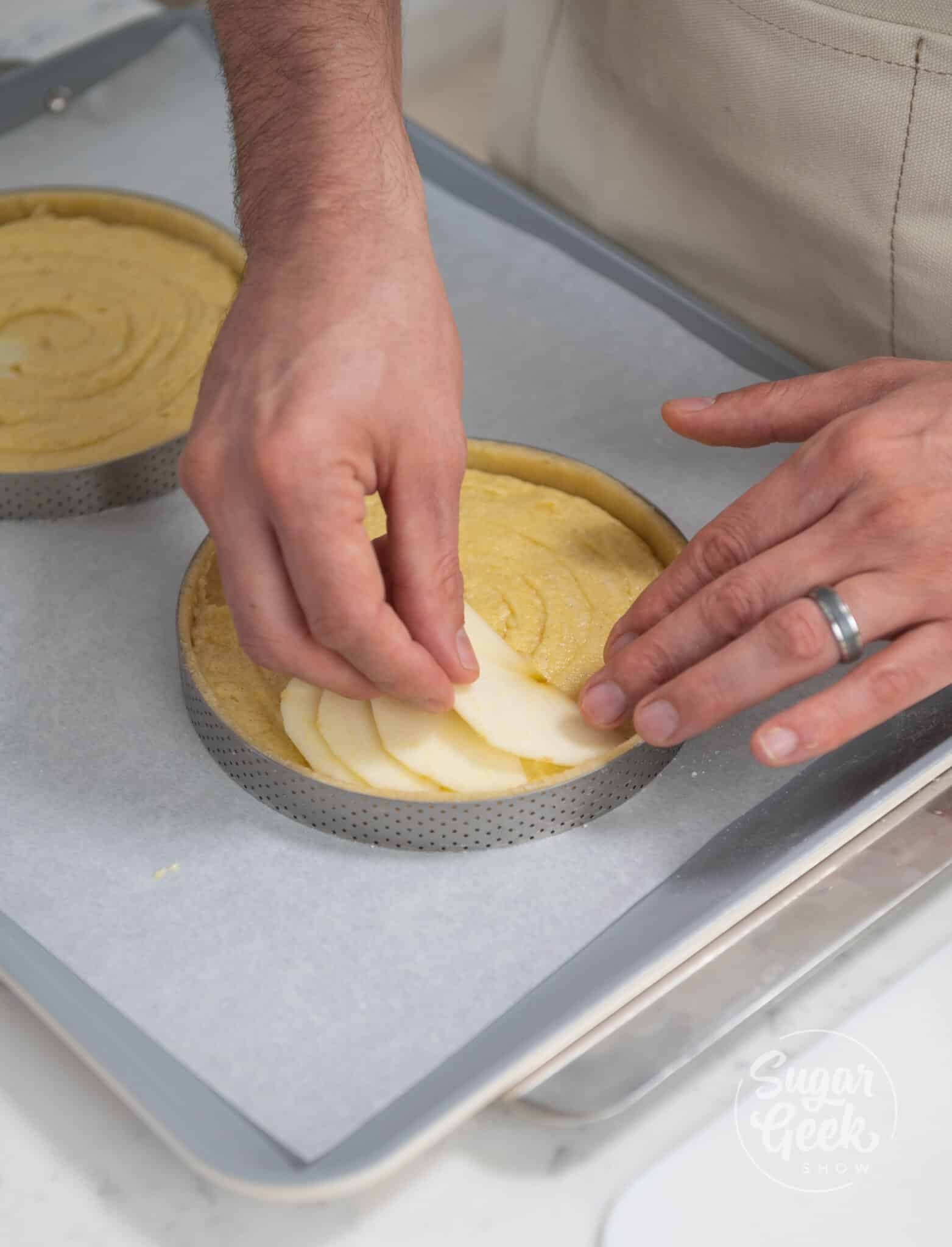 Hands placing apple slices nicely into tart.