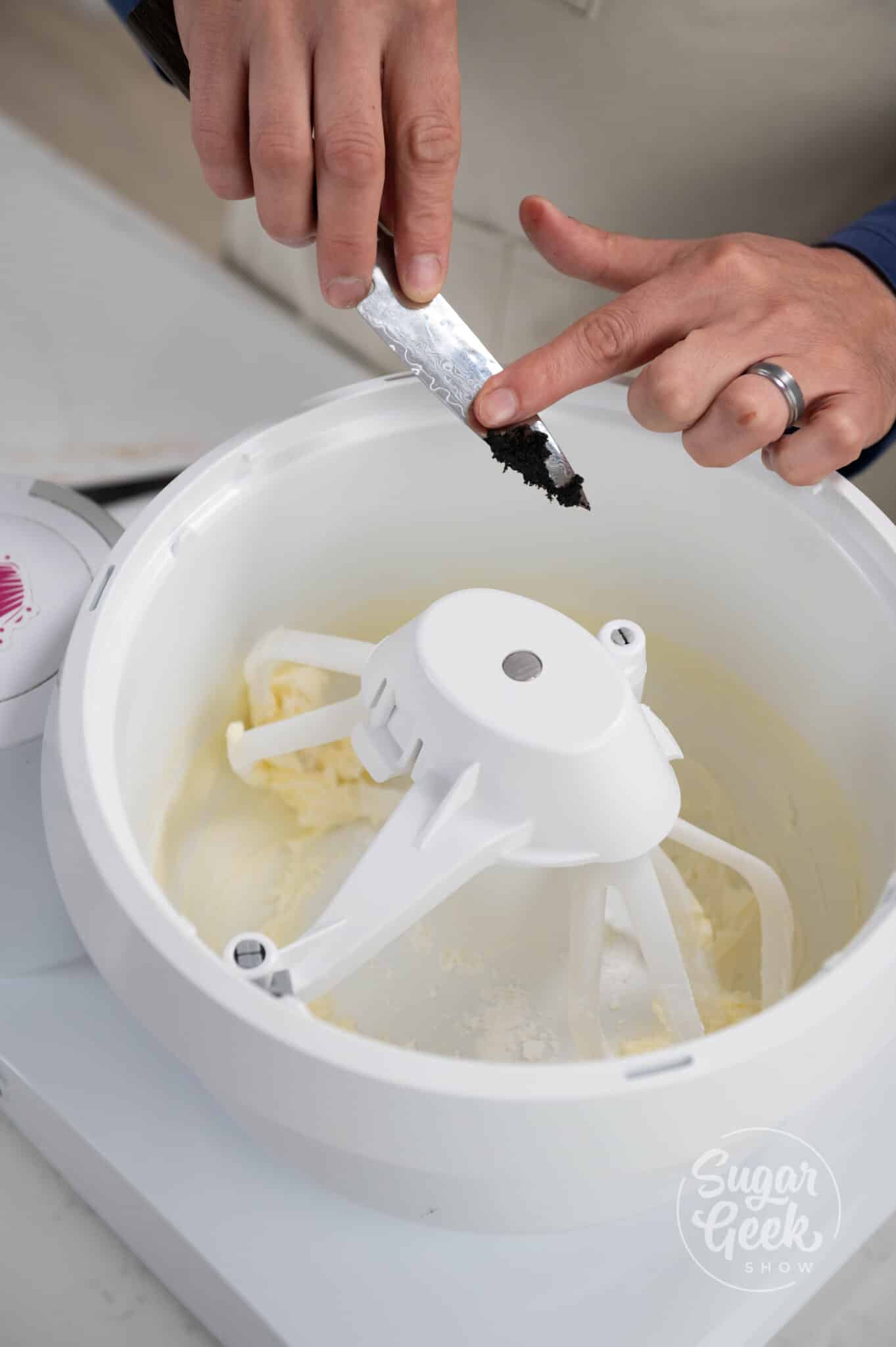 hands holding a knife covered in vanilla to scrape and add vanilla to the bowl.