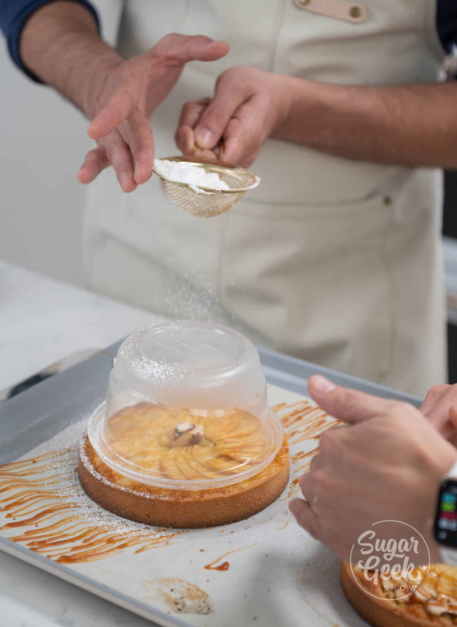 hand sifting powdered sugar with sifter on top of tart.