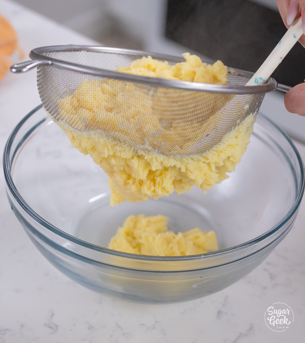 picture of straining cooked pastry cream mixture through a sieve into a bowl with a spatula.